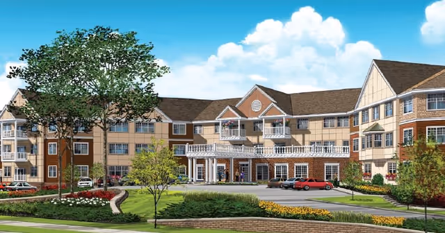 Rendered front view of a three-story assisted living building with balconies, landscaped grounds, and a curved driveway.