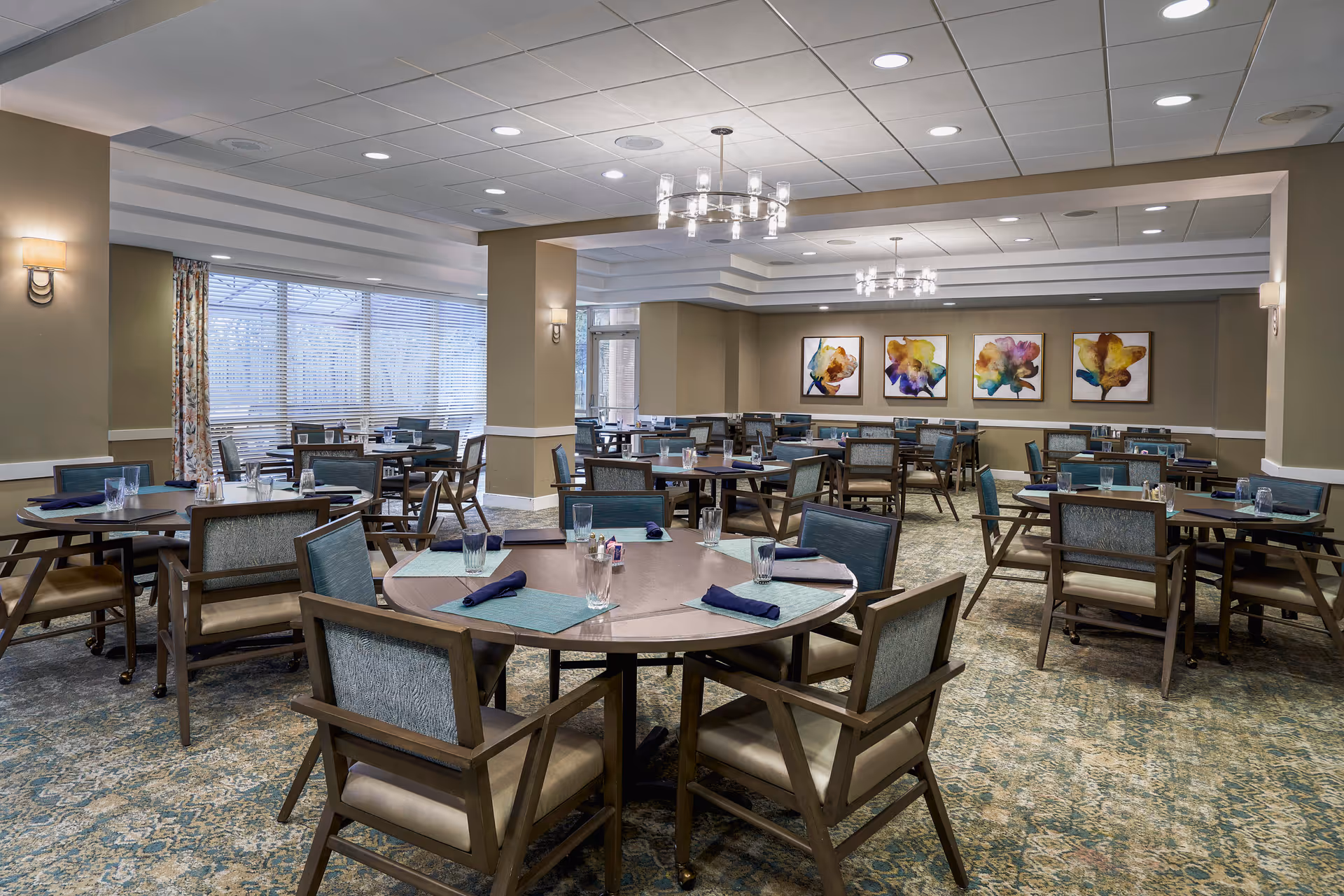 Indoor dining room with round tables set for meals in a senior living facility.