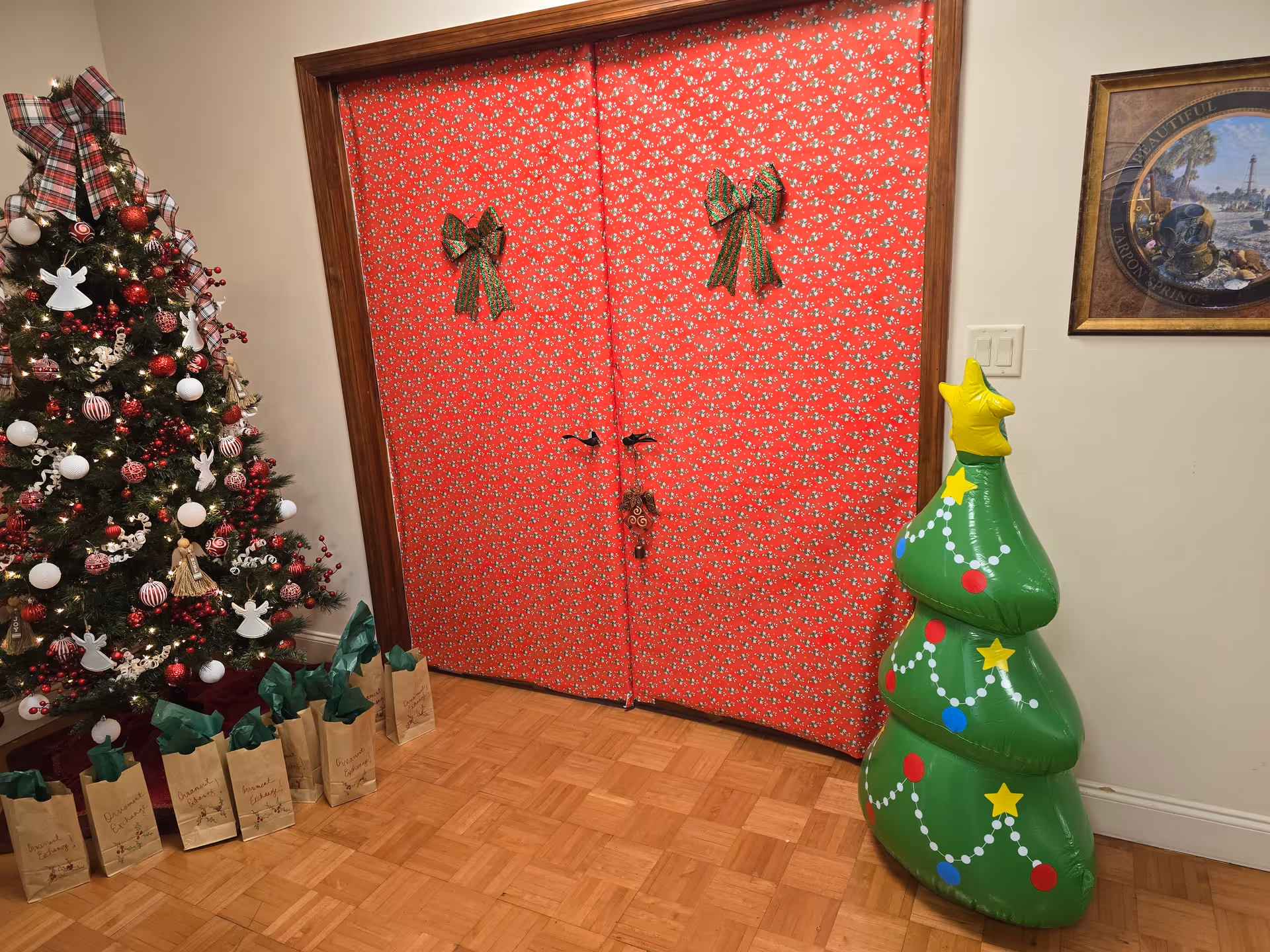 Festive indoor scene with a Christmas tree, gift bags, and a red patterned double door.