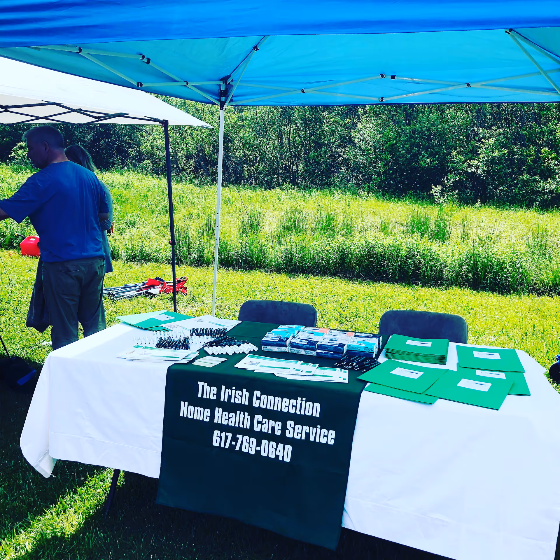 Outdoor information booth under blue tents with promotional materials on a grassy field.
