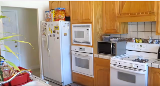 Bright kitchen with wooden cabinets, white appliances, microwave, stove, and a potted plant.