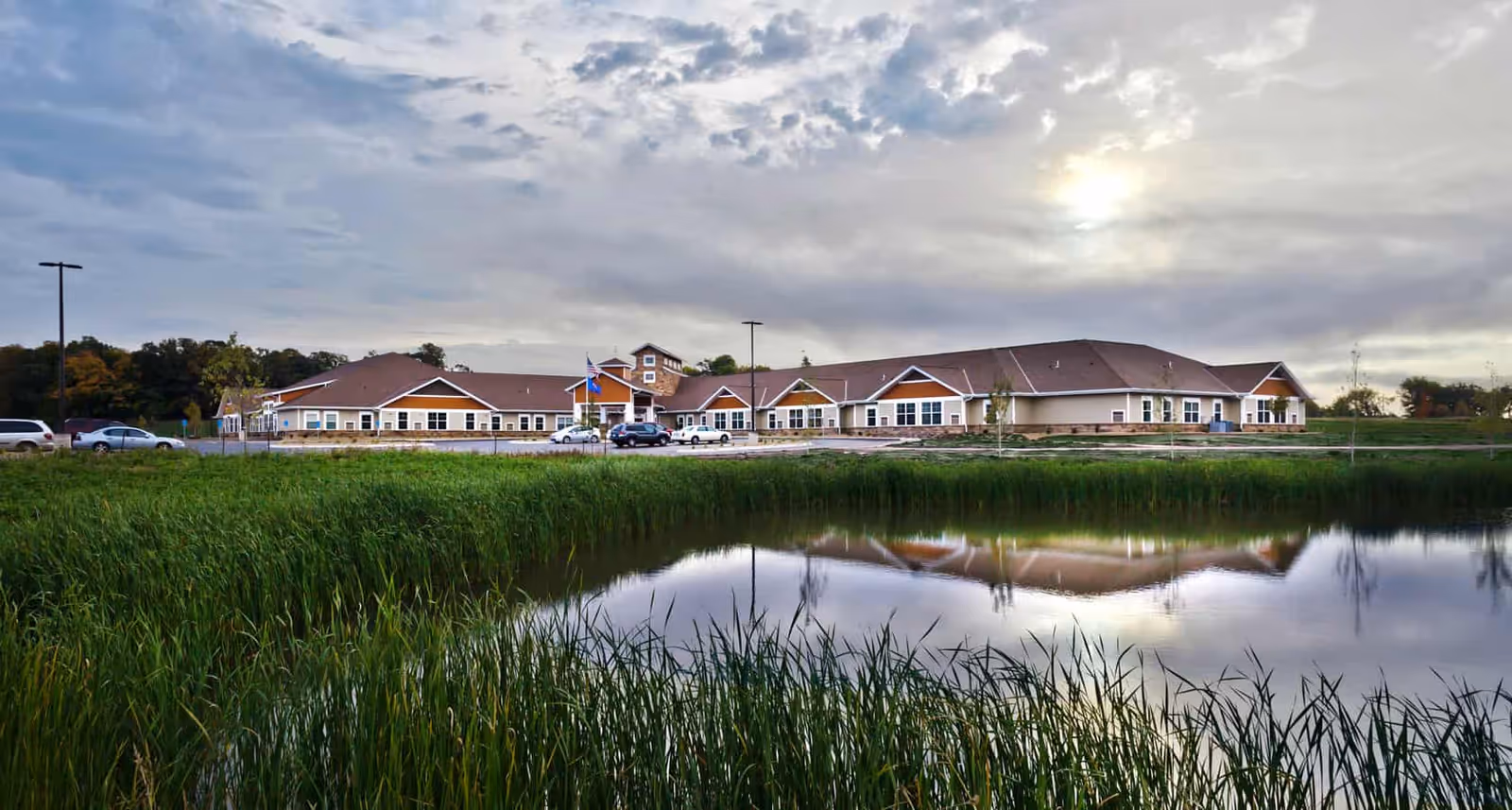 Exterior view of Meadow Place Assisted Living beside a pond and grassy shoreline.