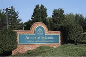 Brick sign reading Arbors at Sylvania, Subacute and Rehabilitation Center, with trees around.