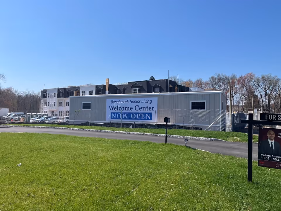 Exterior view of Benchmark Senior Living Welcome Center with NOW OPEN banner