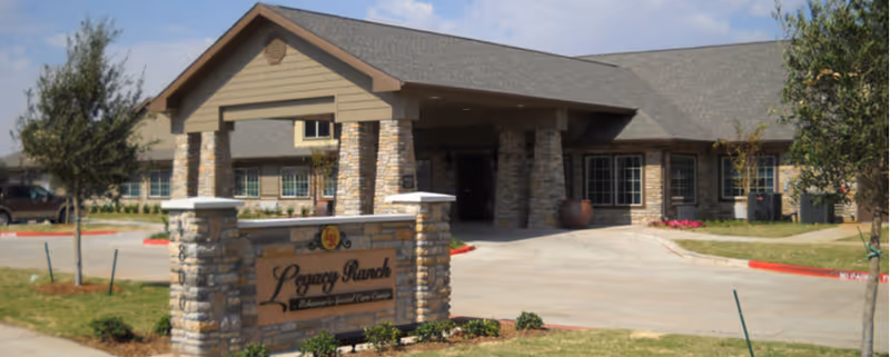Front view of Legacy Ranch senior living facility with stone entrance sign and driveway.