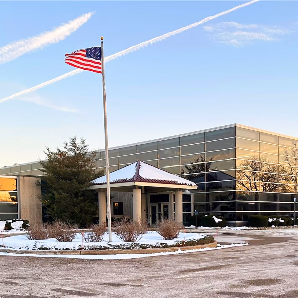 Modern glass-fronted hospital entrance with flagpole and snow-covered landscaping.