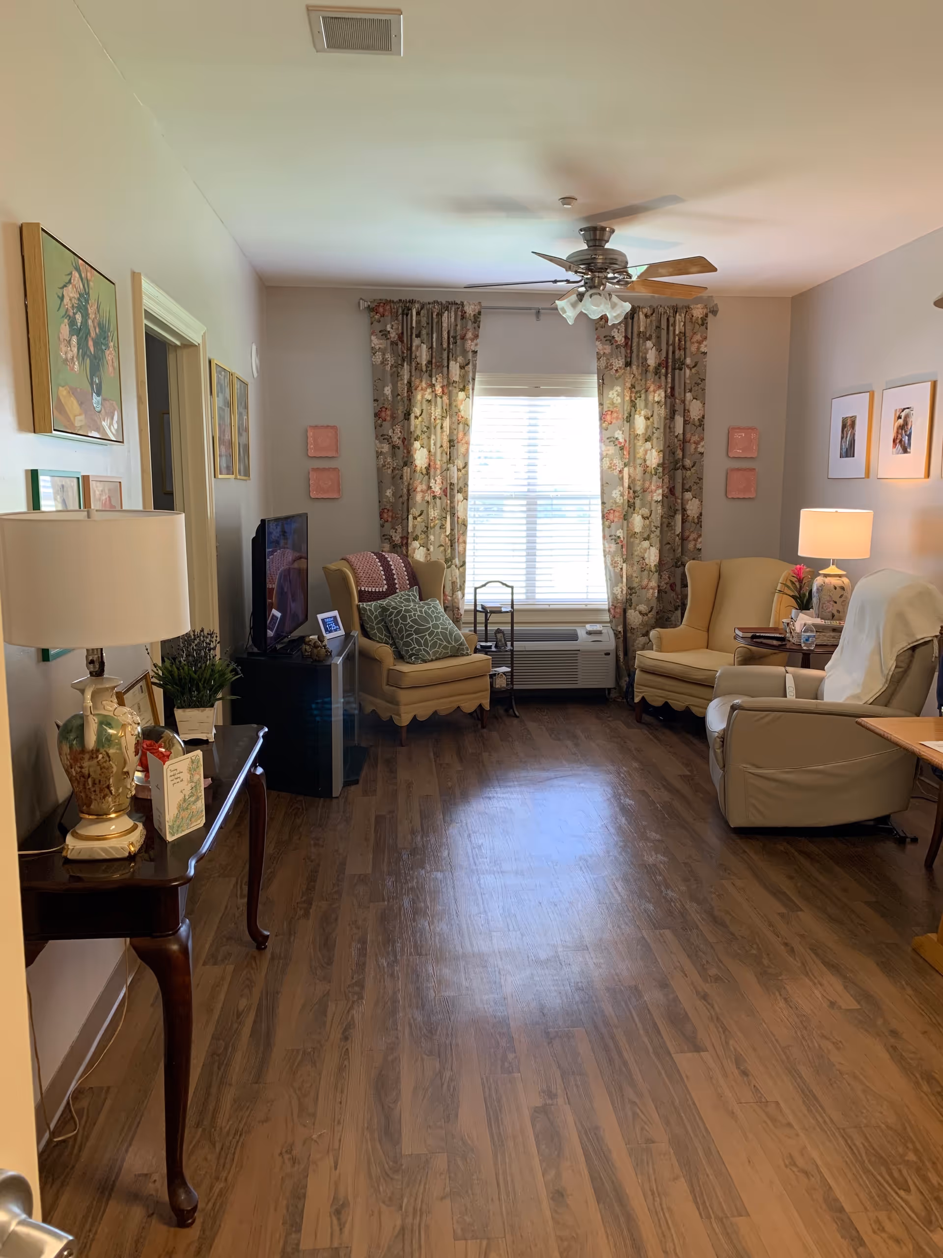 Living room in a senior facility with floral curtains and comfortable seating.