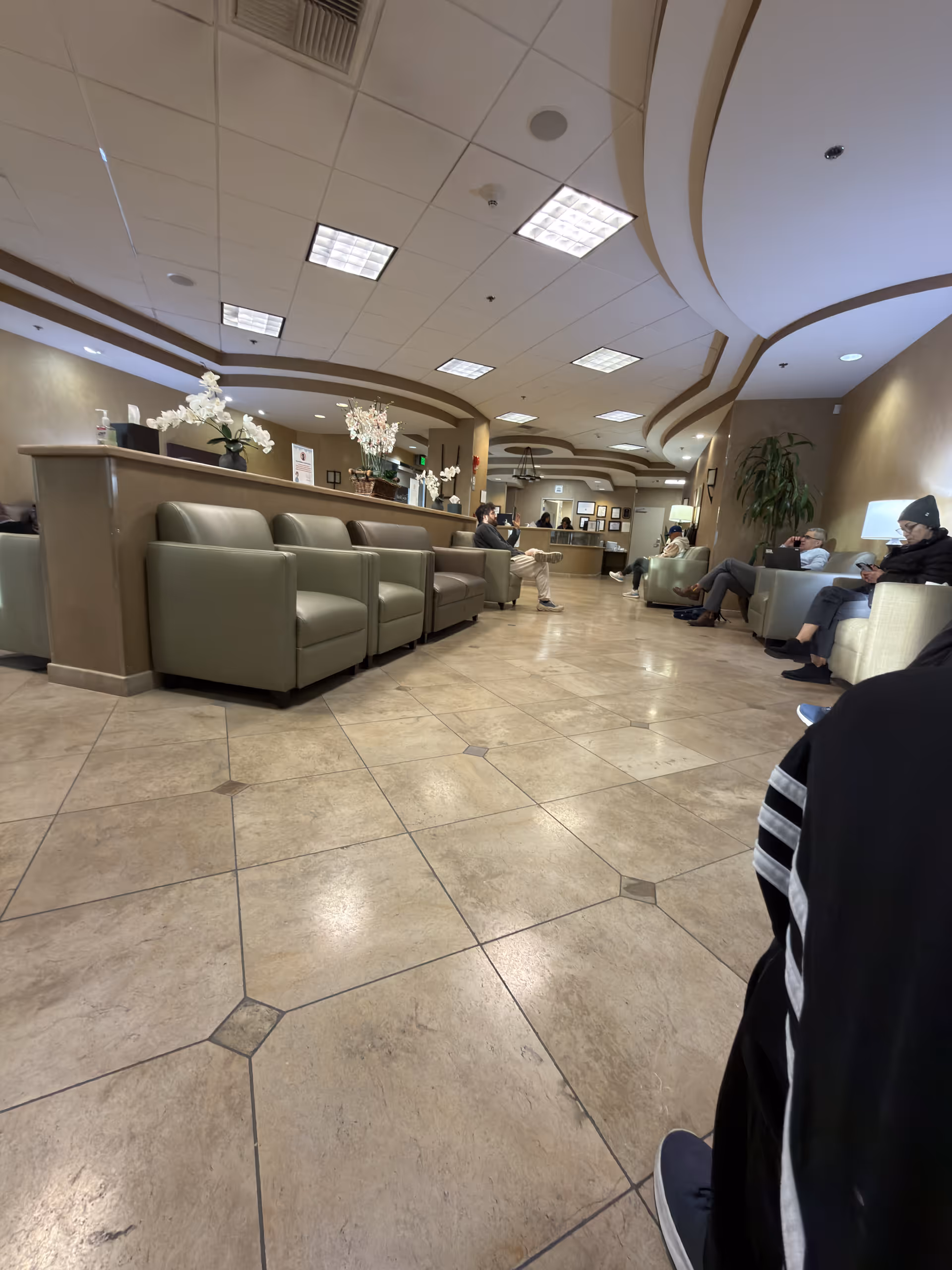 Wide lobby with tan tiled floor, curved ceiling, green couches, and a reception desk.
