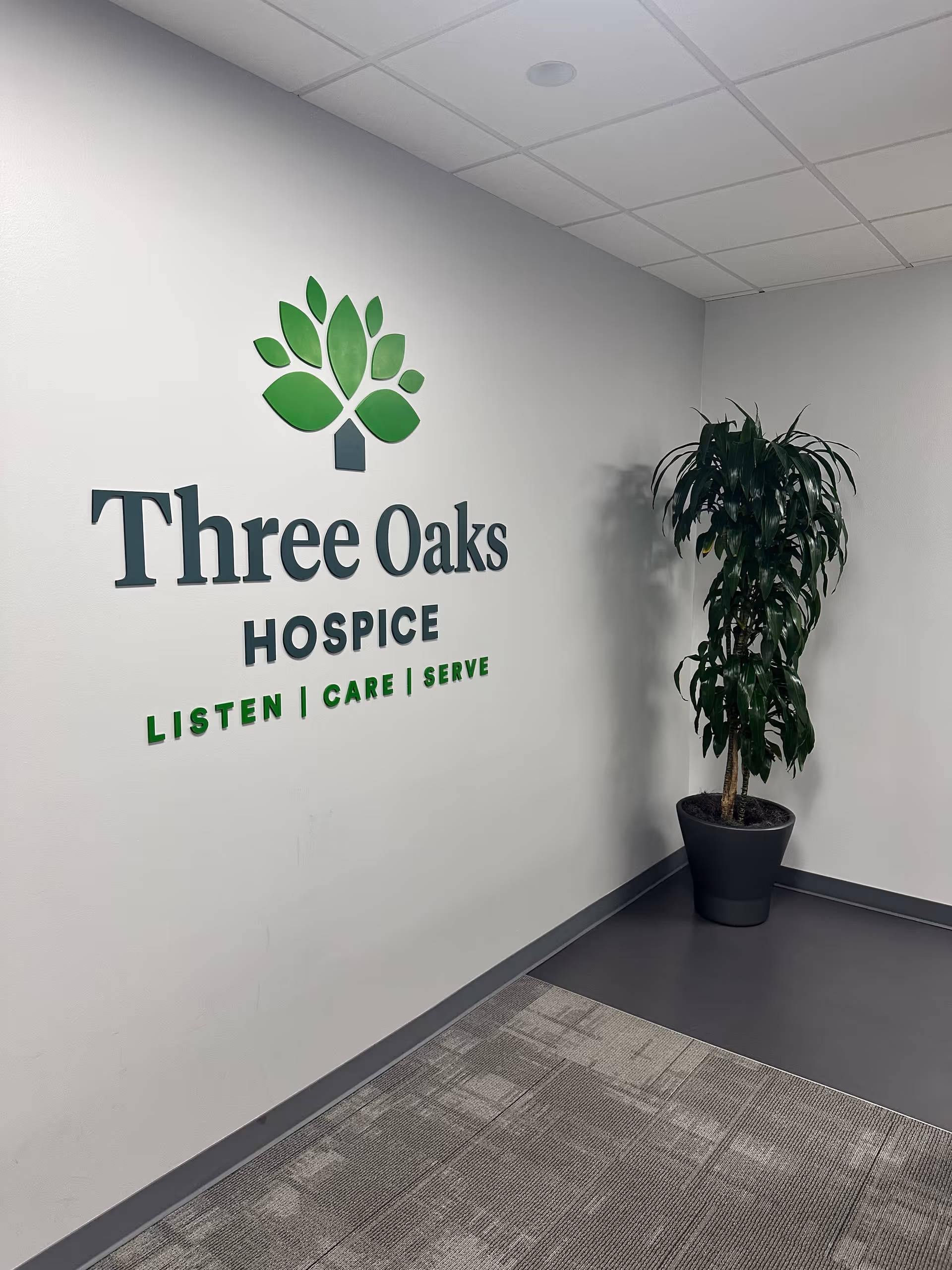 Interior wall featuring Three Oaks Hospice logo, green leaf graphic, and a potted plant.