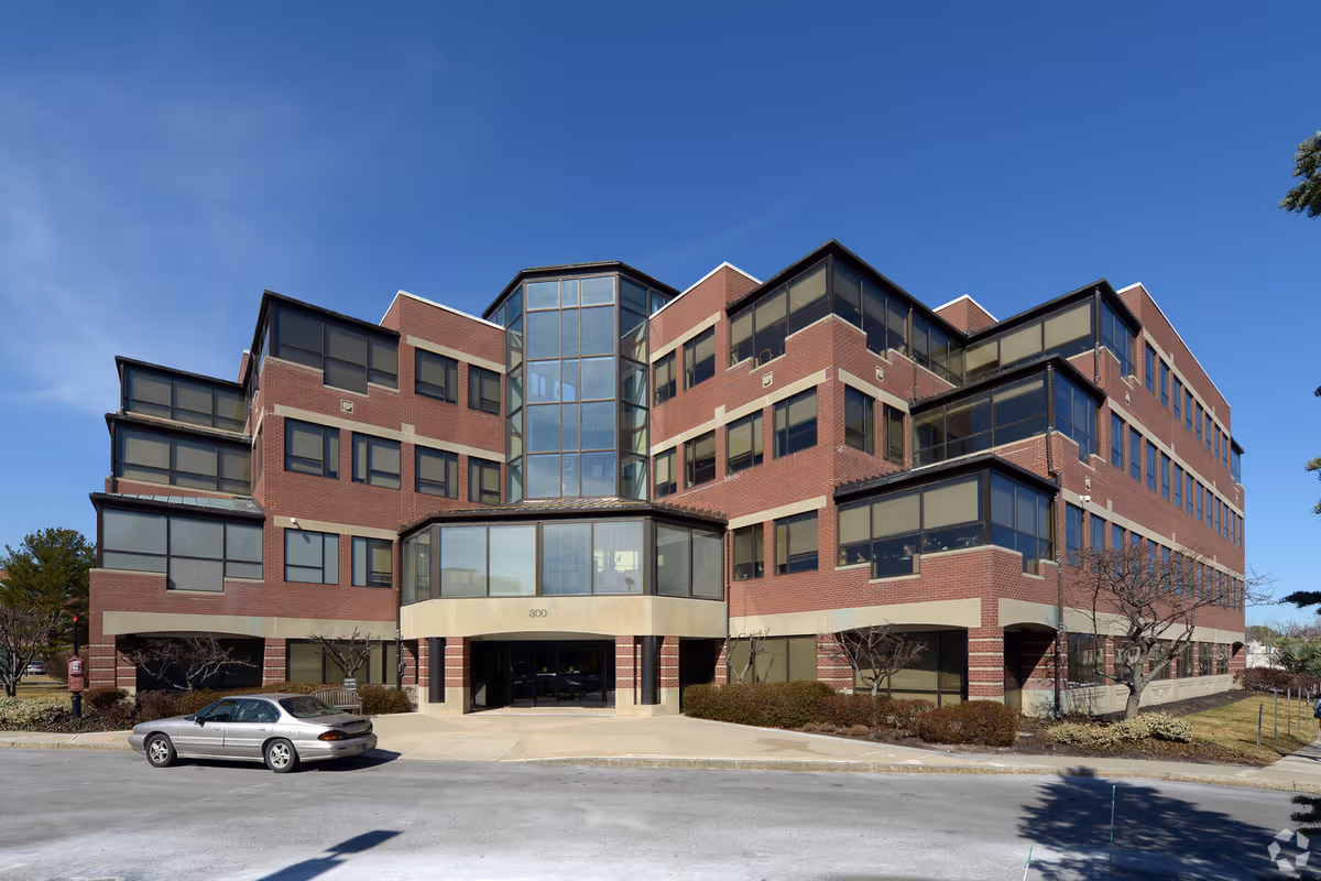 Brick multi-story facility with a glass atrium, modern design, and a car in front.