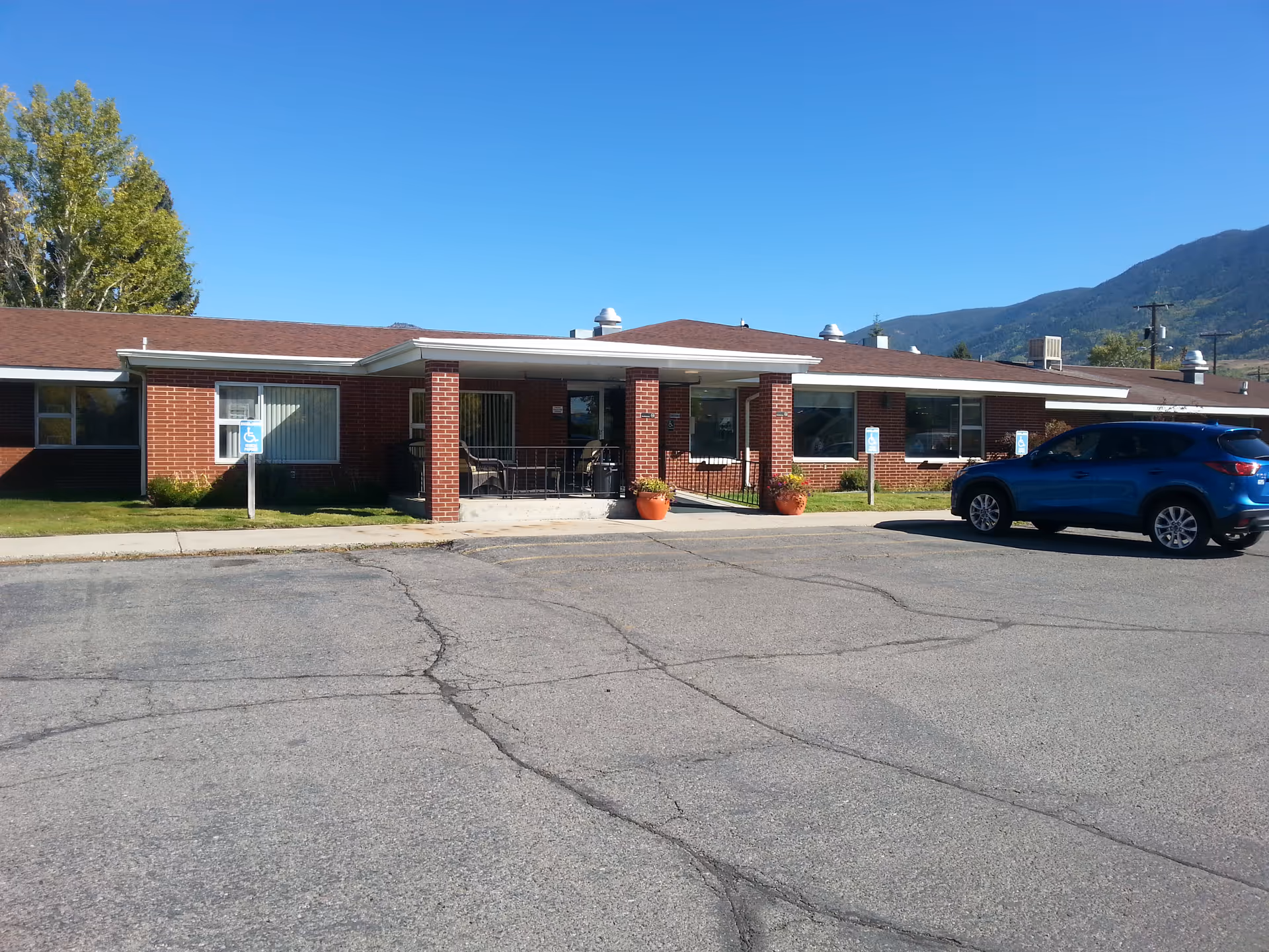 Front view of Crest Nursing Home, a single-story brick building with parked blue SUV.
