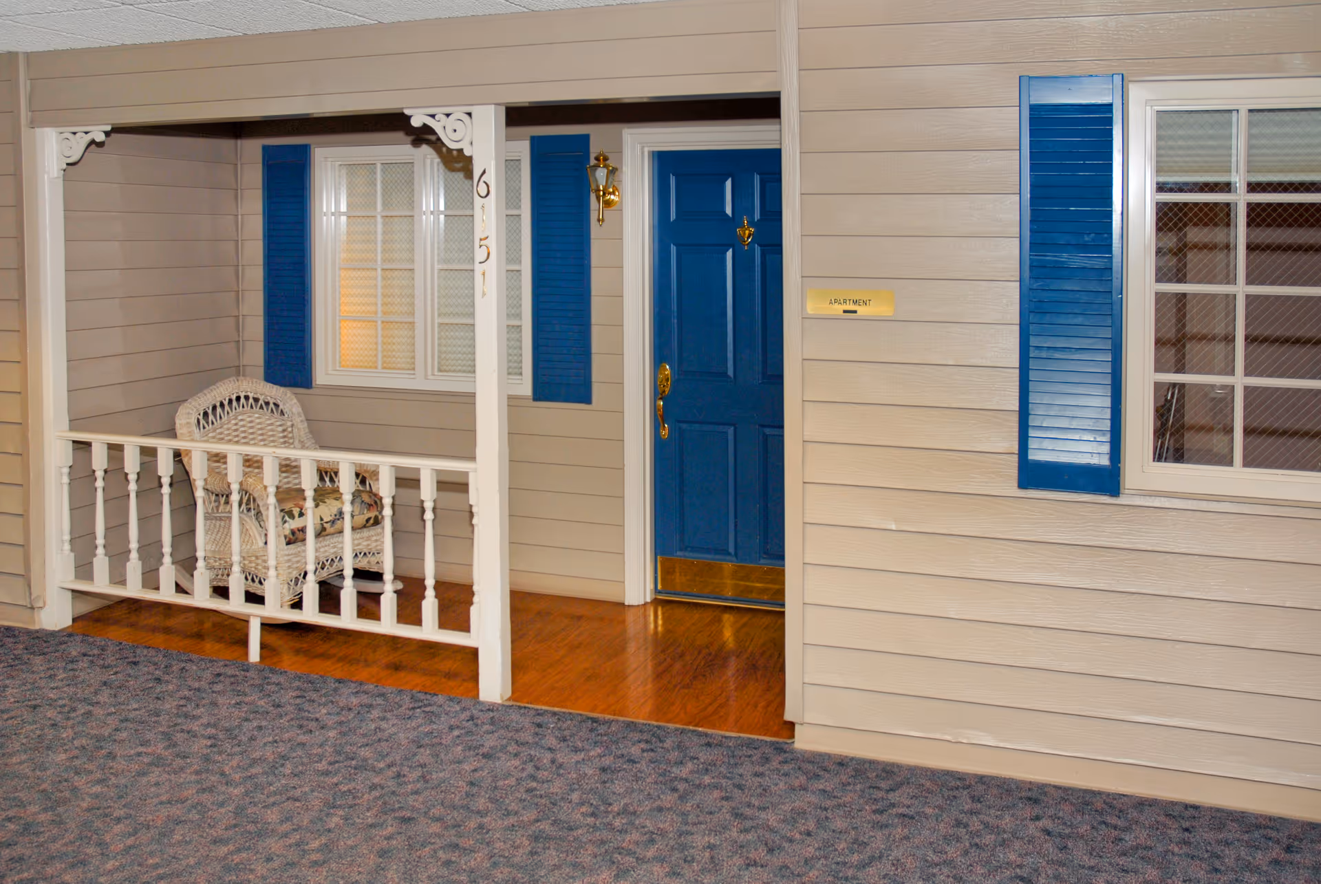 Entrance of a Life Care Center unit with blue door, beige siding, and porch chair.