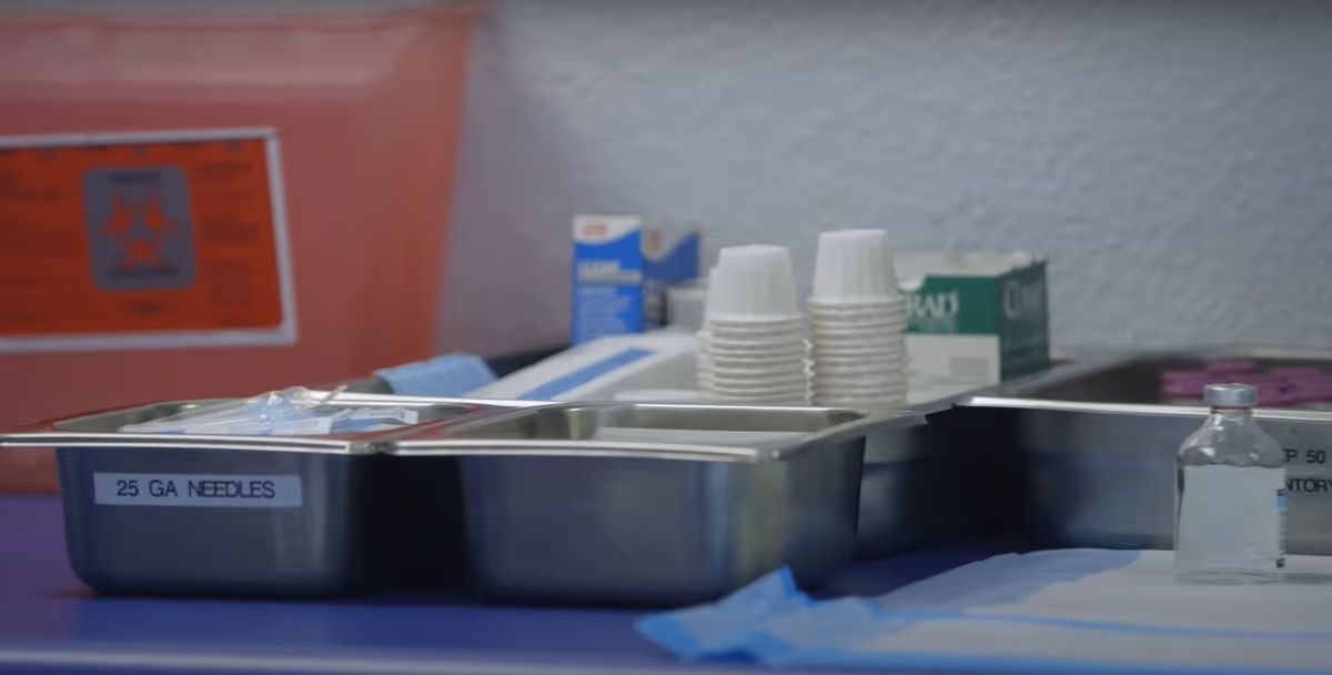 Stainless steel trays with IV supplies, cups, and labeled needles on a table.