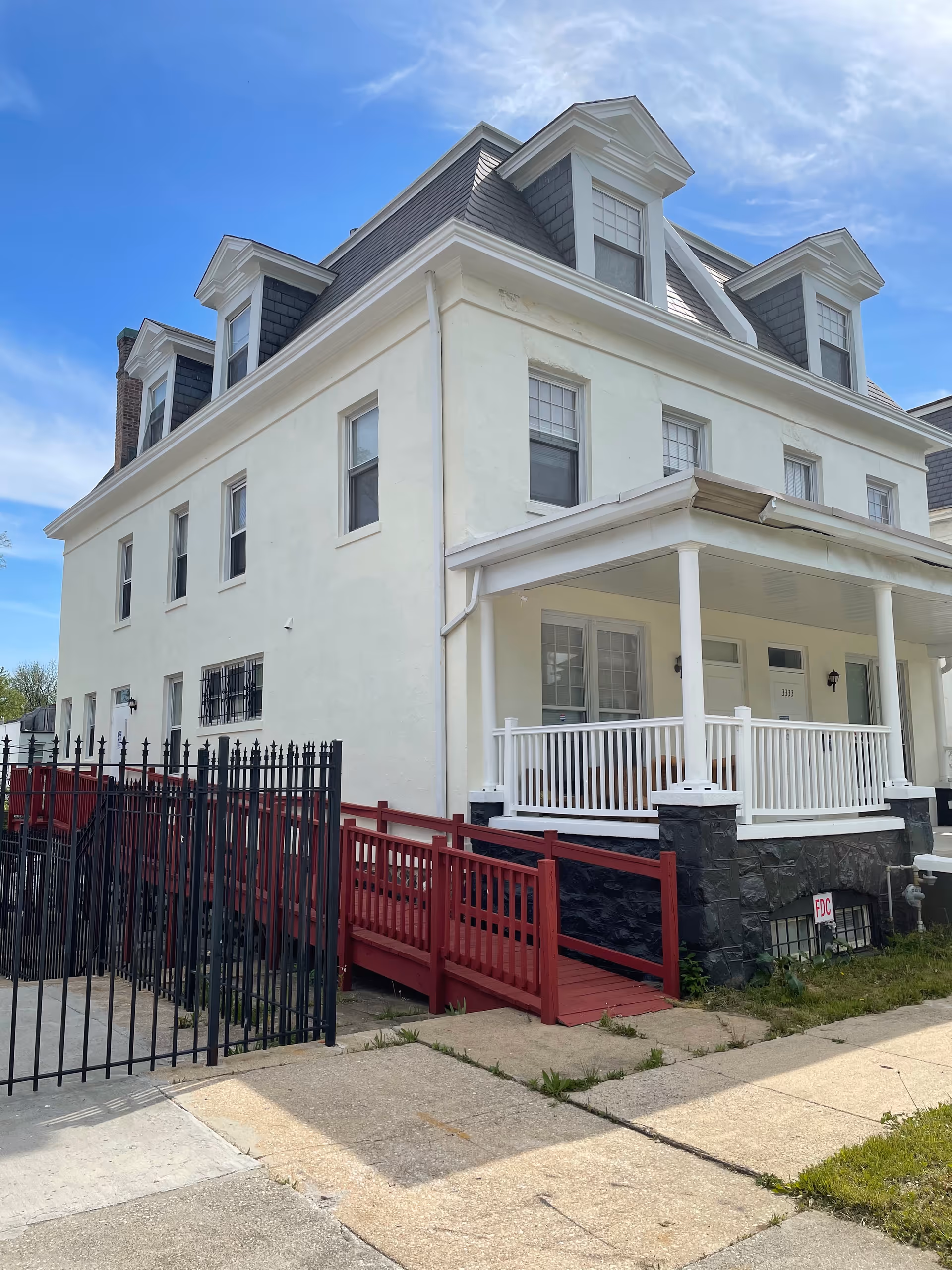 White multi-story assisted living building with front porch, ramp, and black fence.