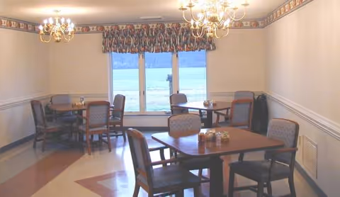 A dining room with several tables and chairs beneath chandeliers by a large window.