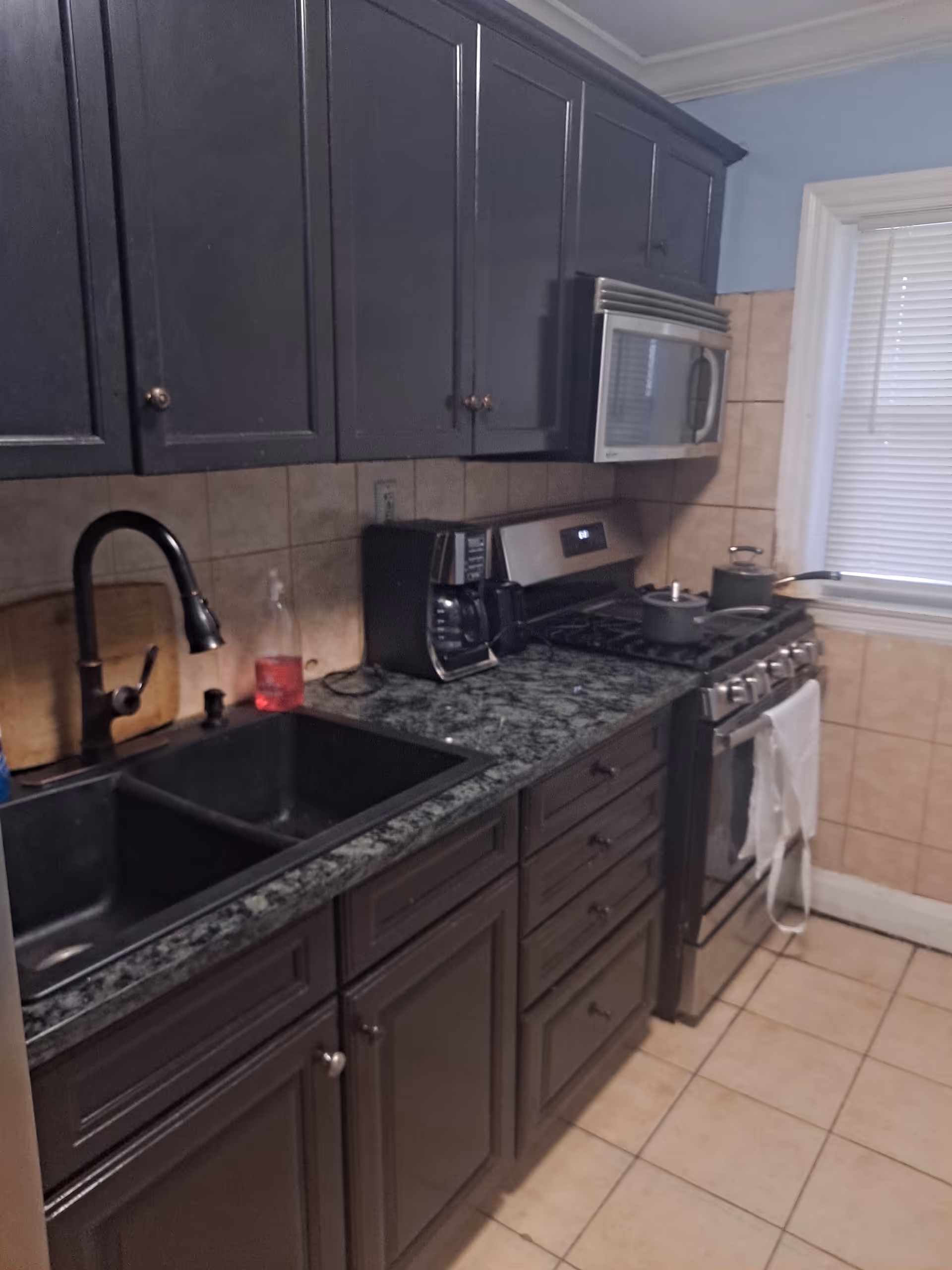 Dark cabinets, granite countertops, and stainless appliances line a compact kitchen.