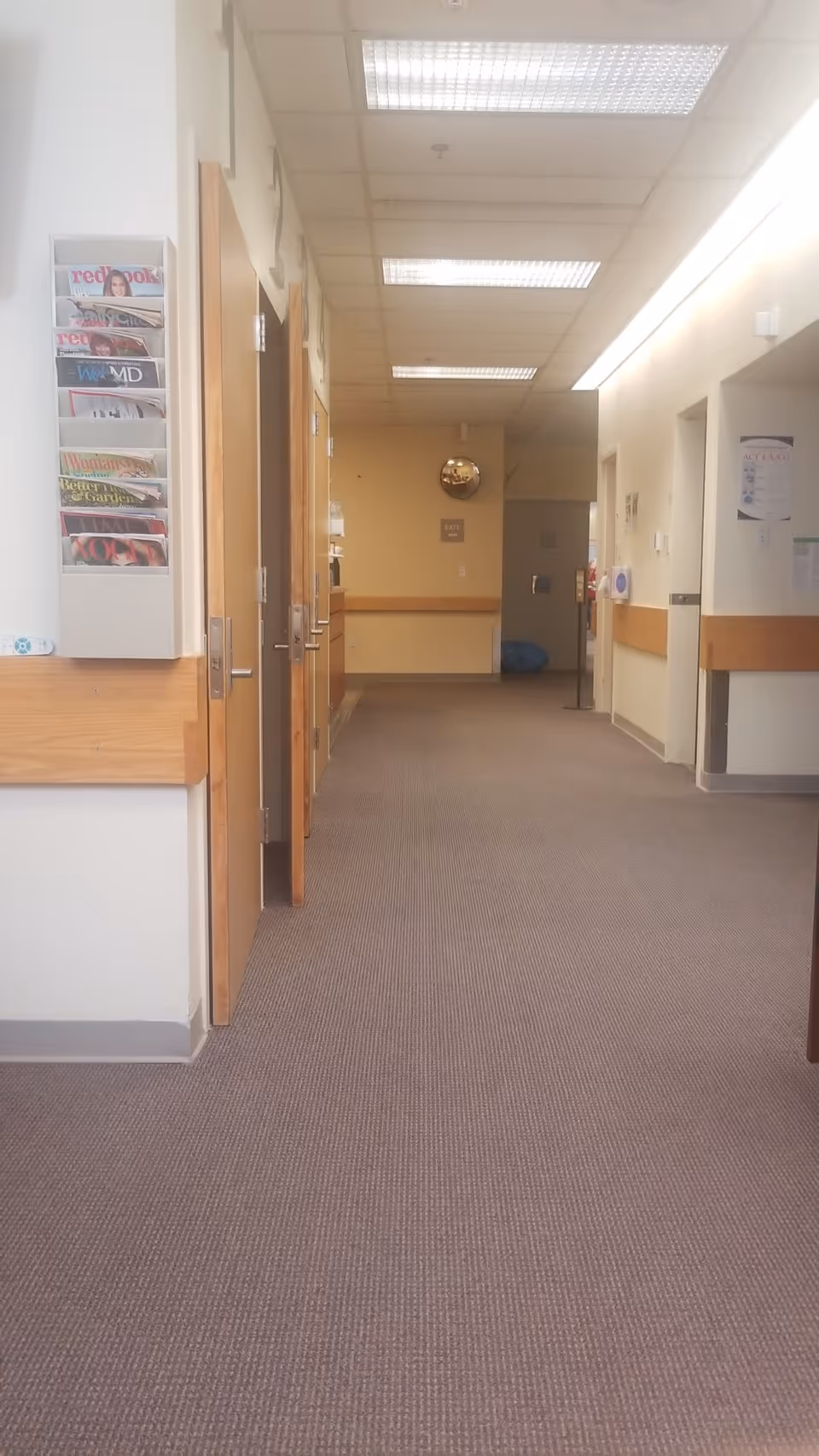 Long corridor in a senior living facility with doors, a magazine rack, and overhead fluorescent lights.