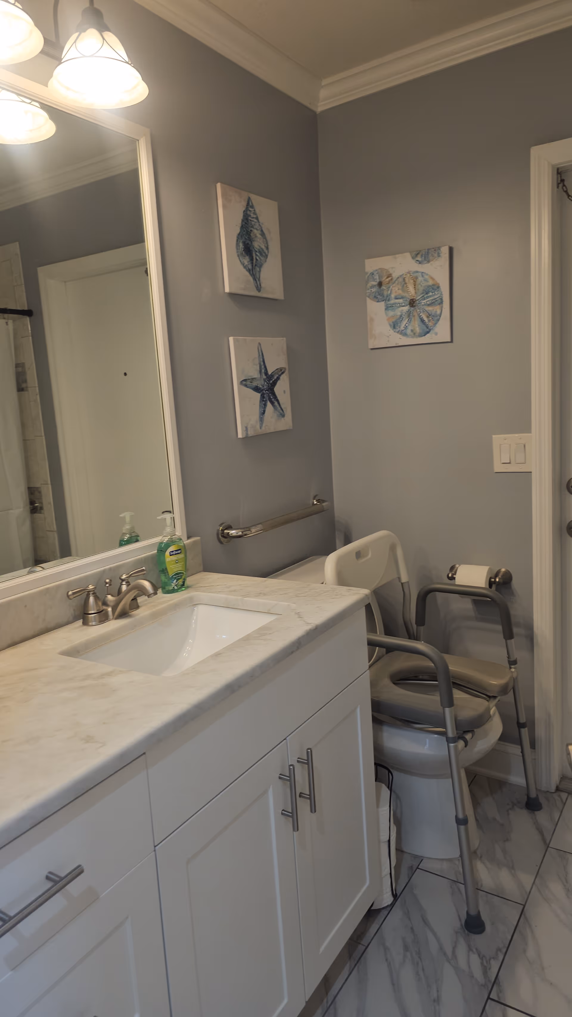 An accessible bathroom features a sink, mirror, grab bar, toilet, and mobility chair.