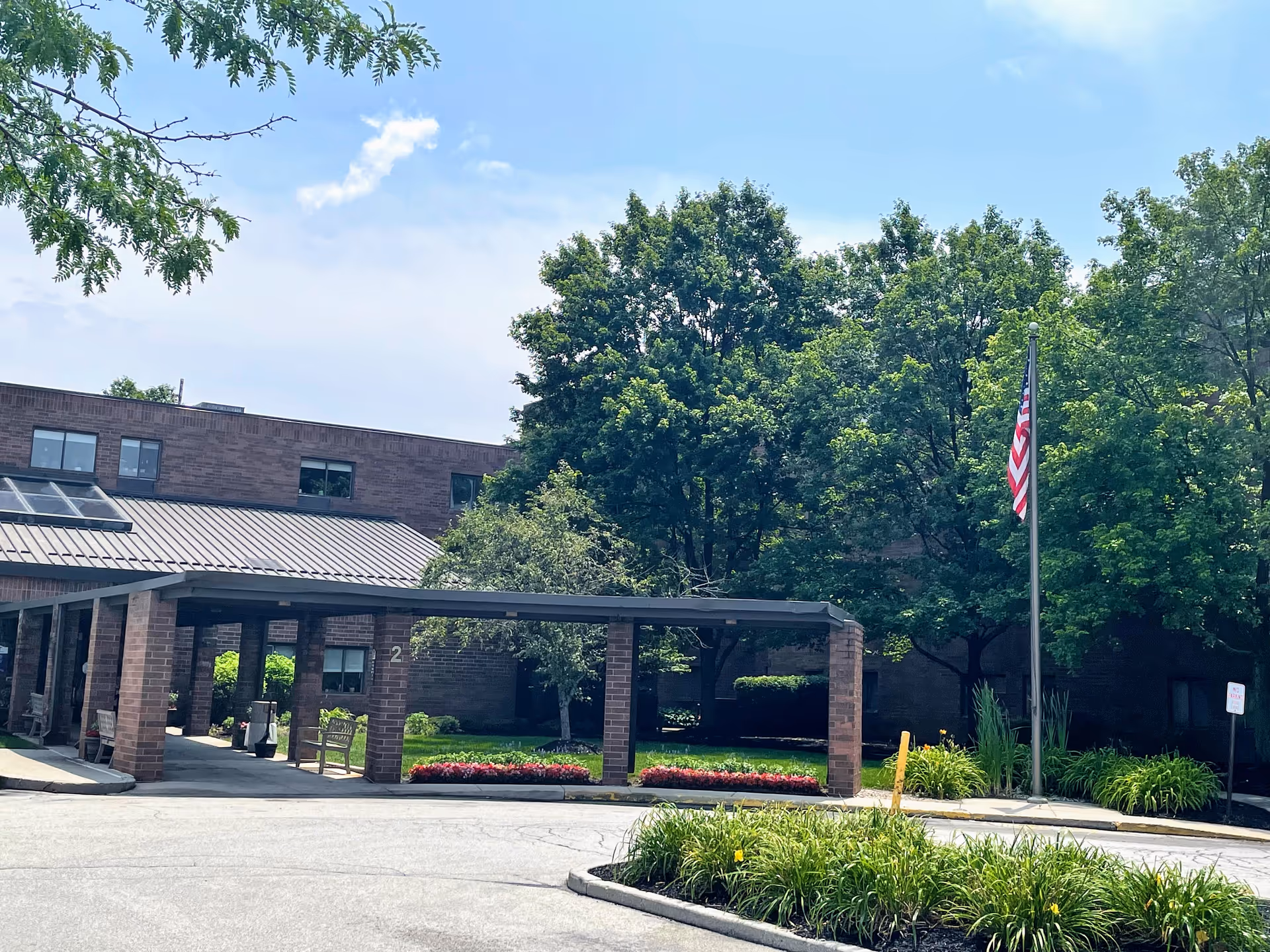 Exterior view of Majestic Care of Carmel showing entrance canopy, flagpole, and landscaped surroundings.