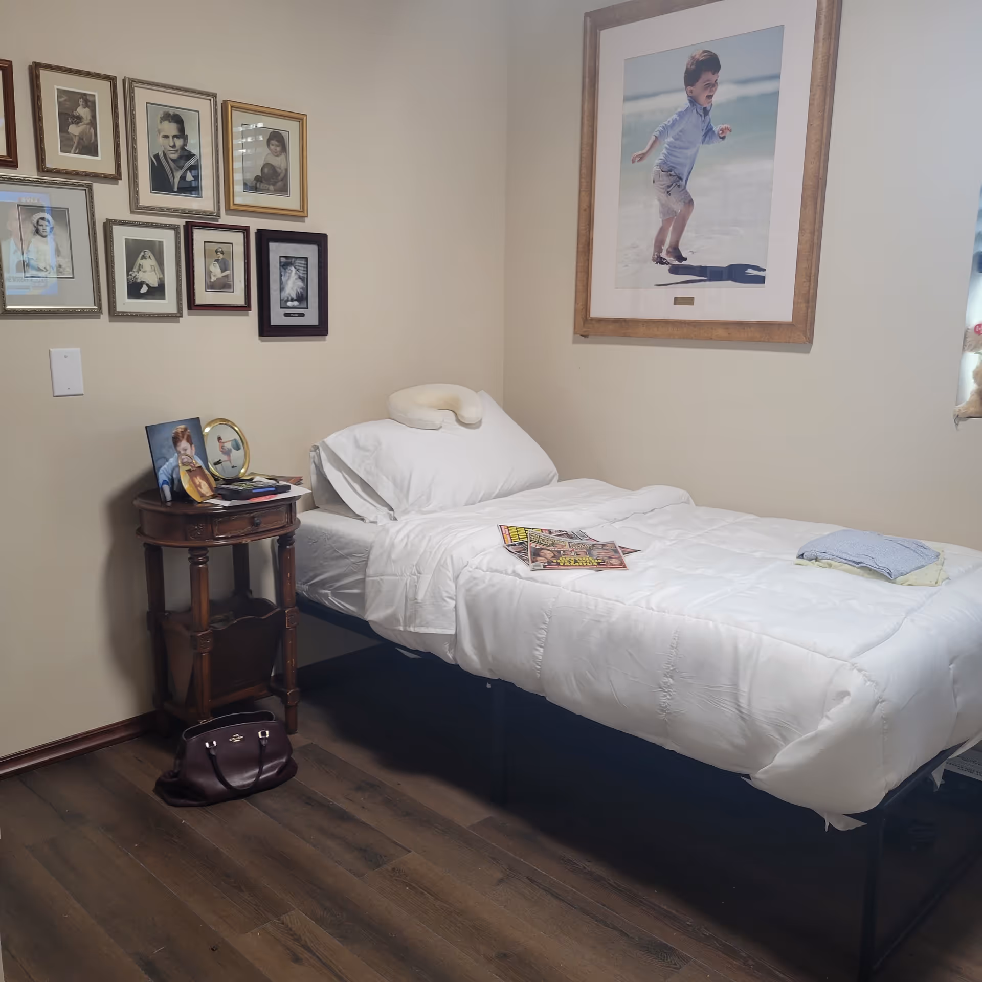Single bed with white bedding, framed photos on wall, and a side table in a bedroom.