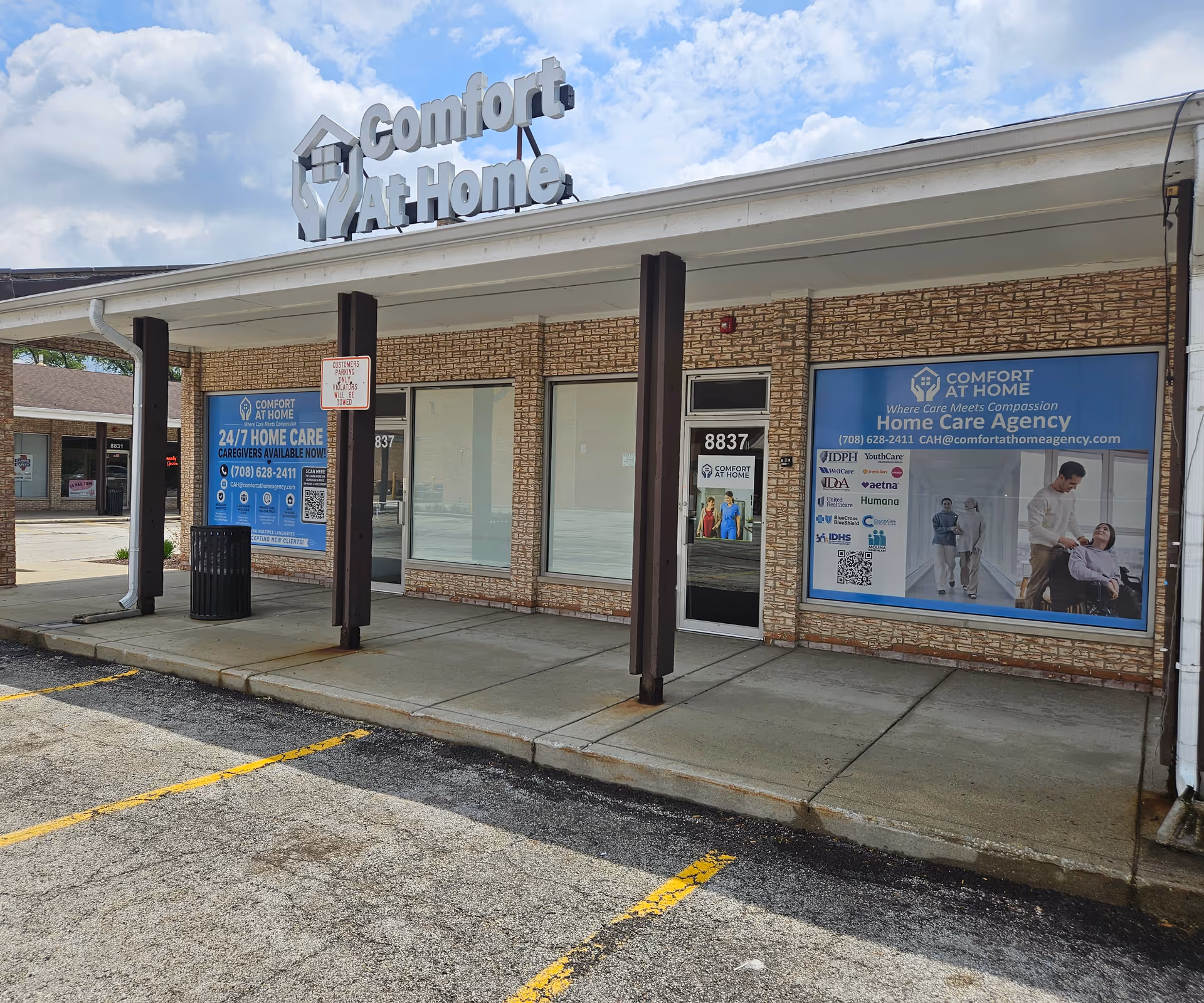 Exterior view of Comfort At Home LLC storefront with large blue banners in windows.