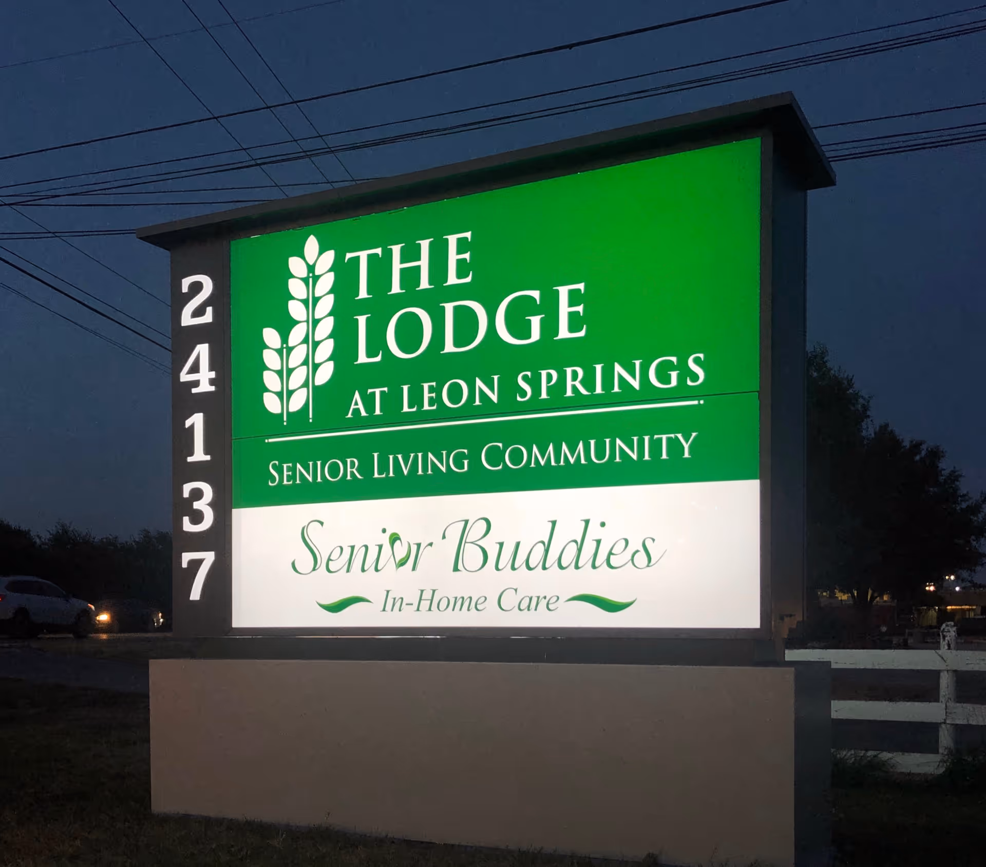 Green illuminated sign reads The Lodge at Leon Springs Senior Living Community Senior Buddies In-Home Care