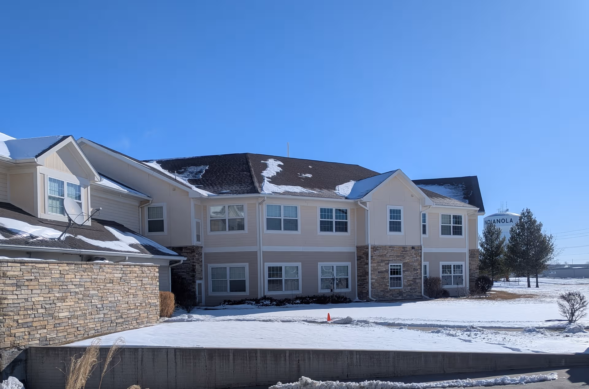 Two-story beige senior living building with stone accents under a clear blue sky, snow on roof