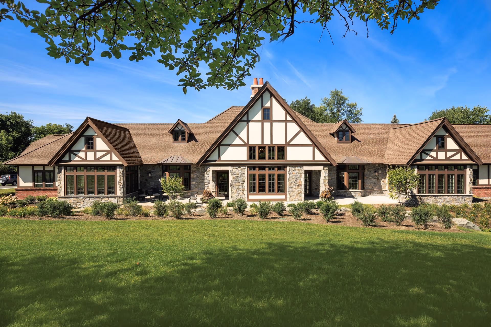 Front exterior of Loudonville Assisted Living Residence with a Tudor-style façade, manicured lawn, and blue sky.