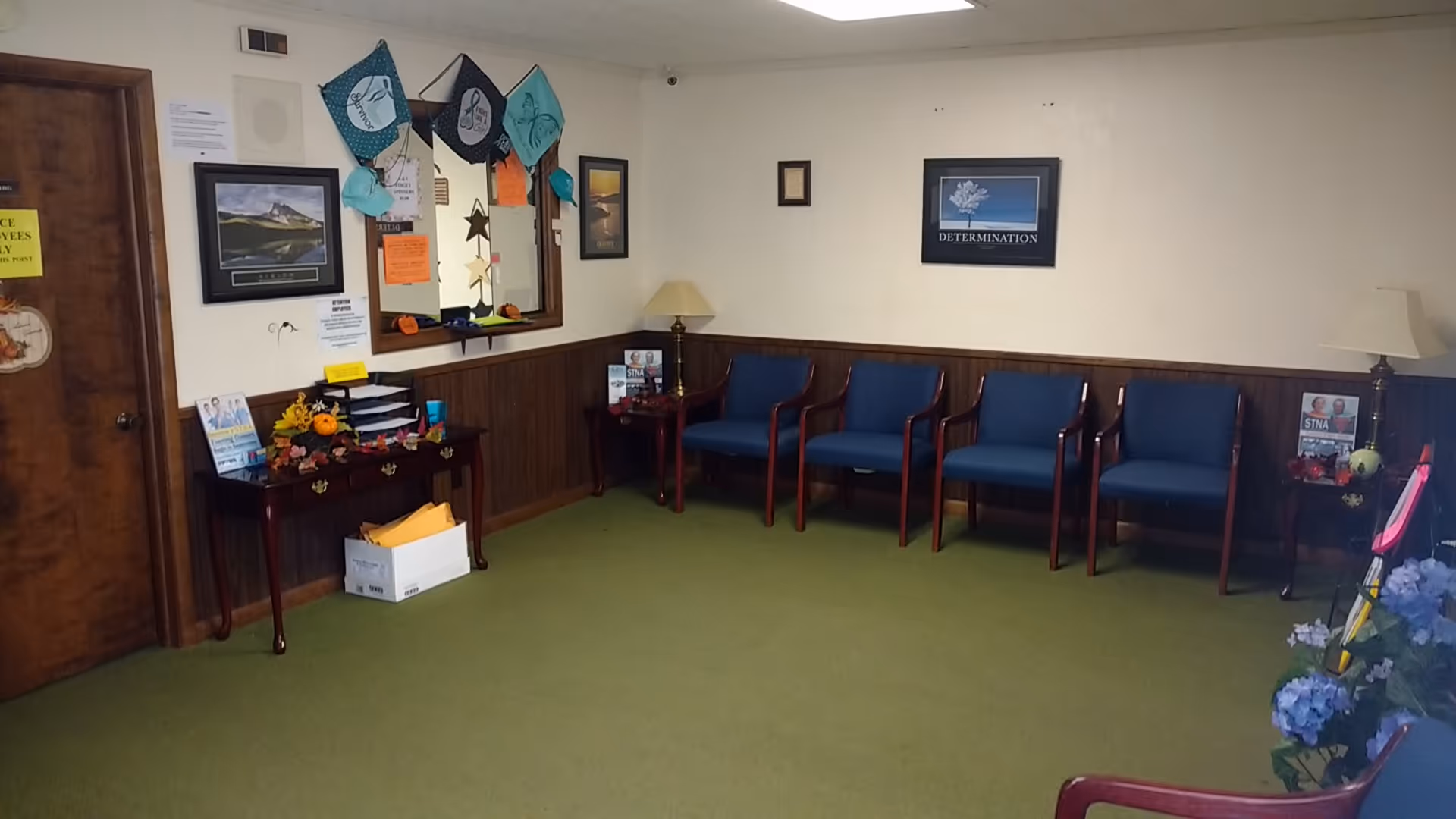 A small waiting area with blue chairs along a wood-paneled wall and green carpet.