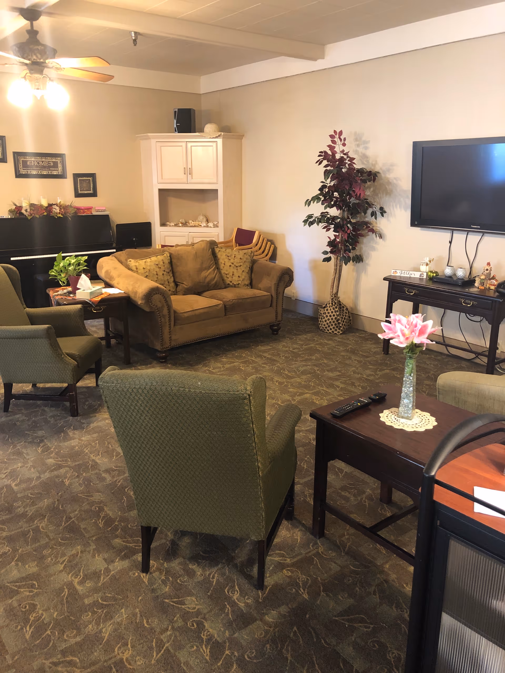 Cozy senior living lounge with sofa, chairs, piano, TV, and coffee table.