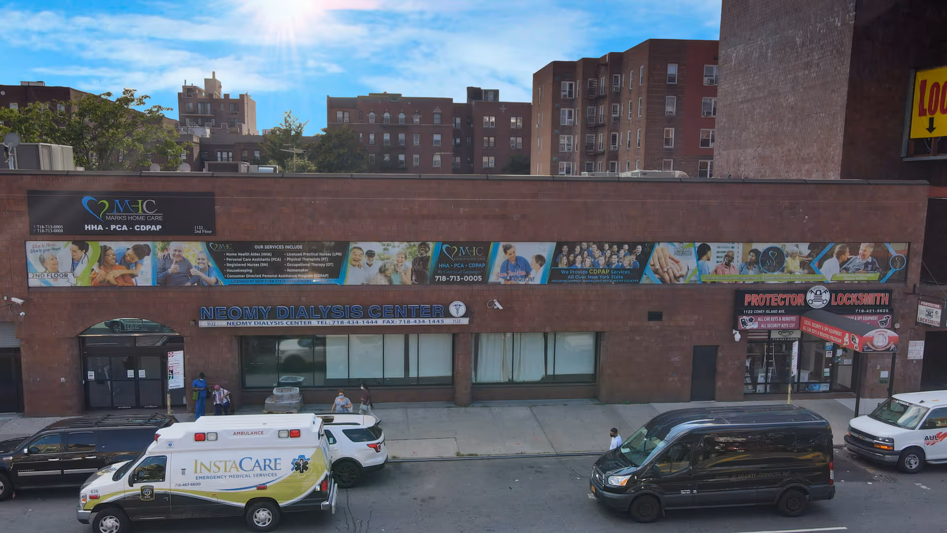 Brick storefront with banners, a dialysis center sign, and several parked ambulances on a city street.