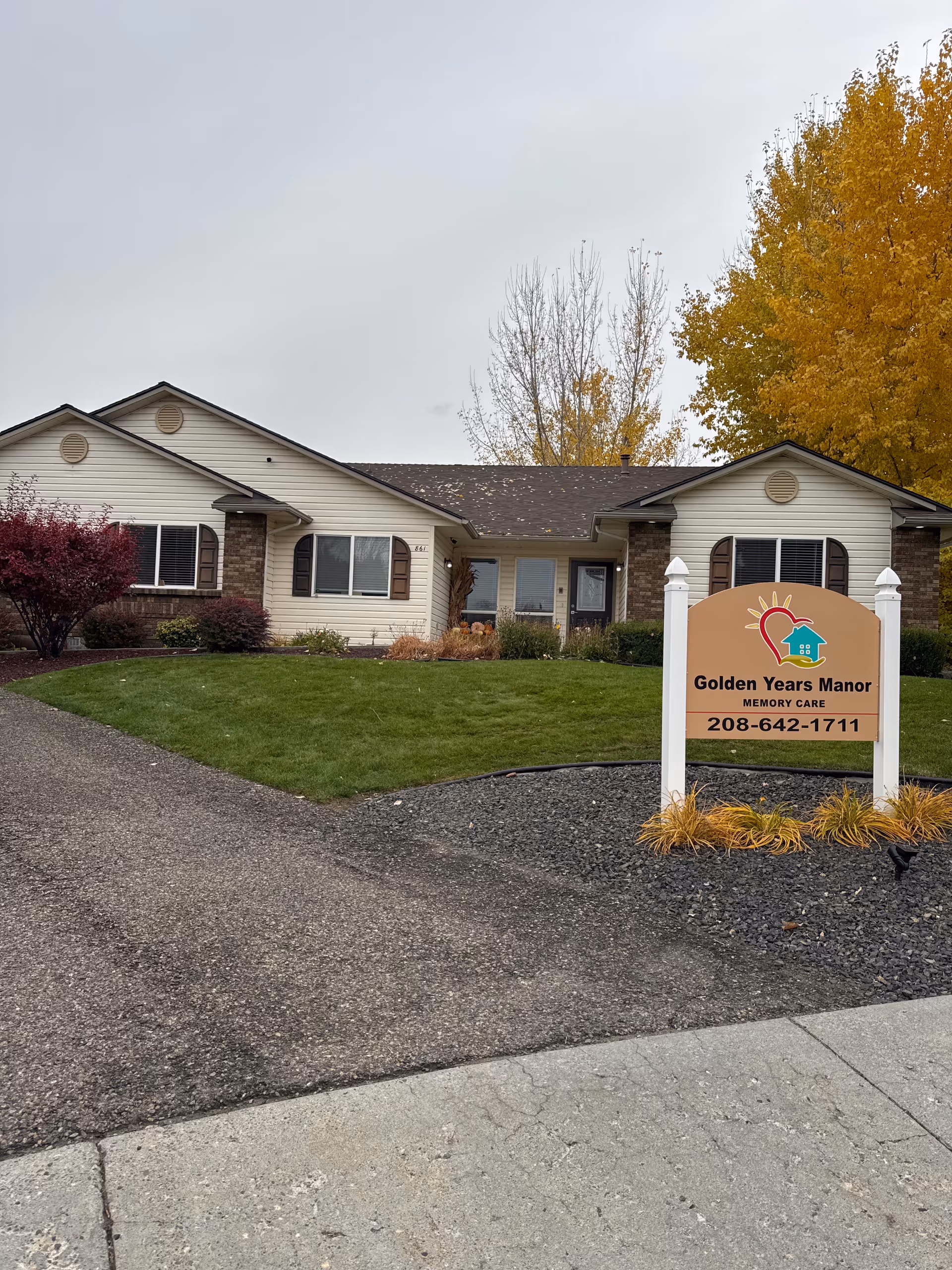 Front view of a single-story memory care facility with a sign and landscaped yard.