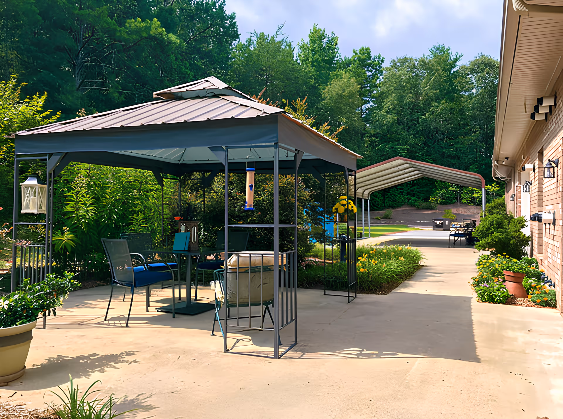 Outdoor patio with a metal gazebo, seating, potted plants, and a walkway alongside a brick building.