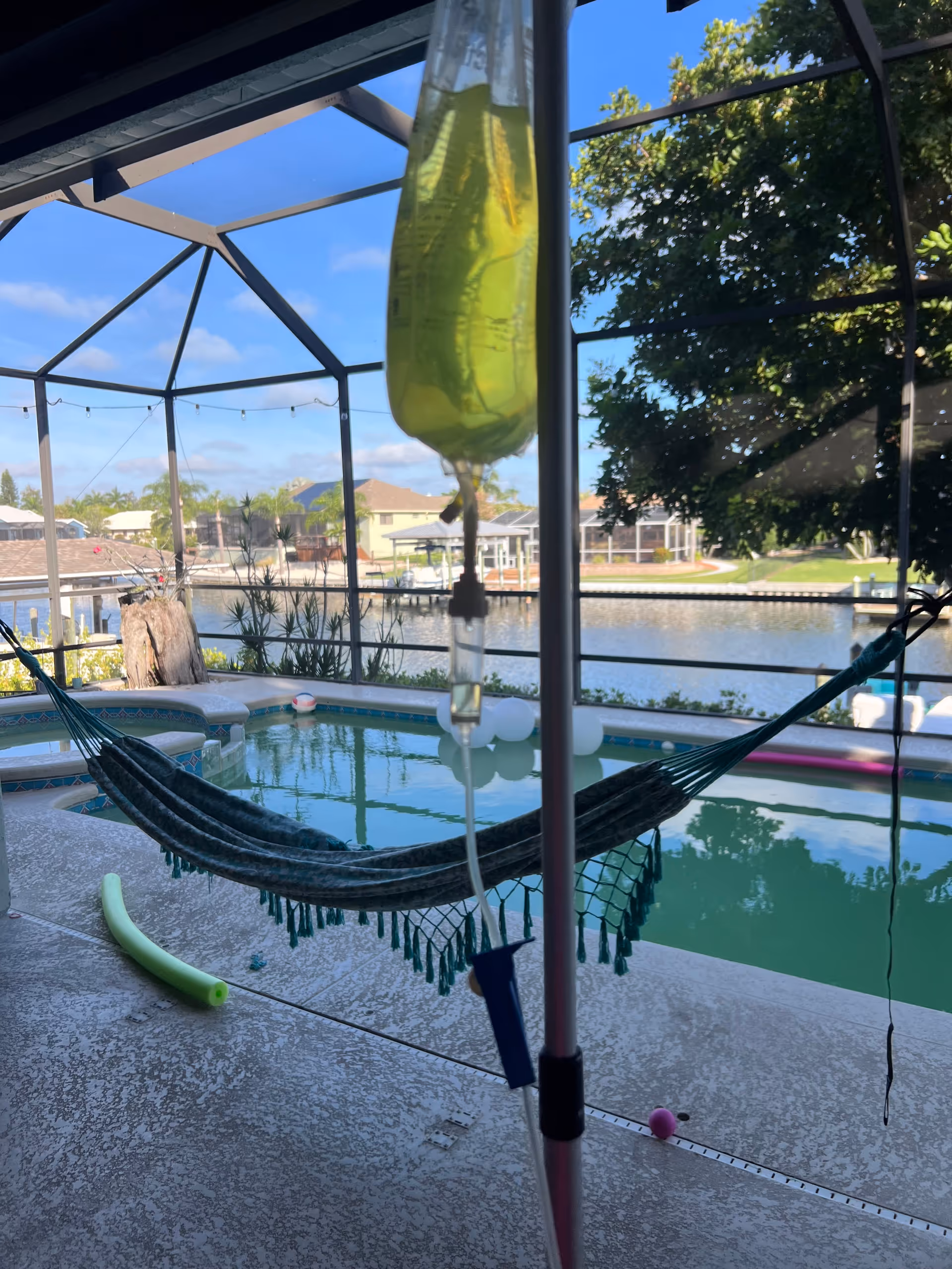 Outdoor pool area with a hammock, IV infusion setup, and waterfront view.