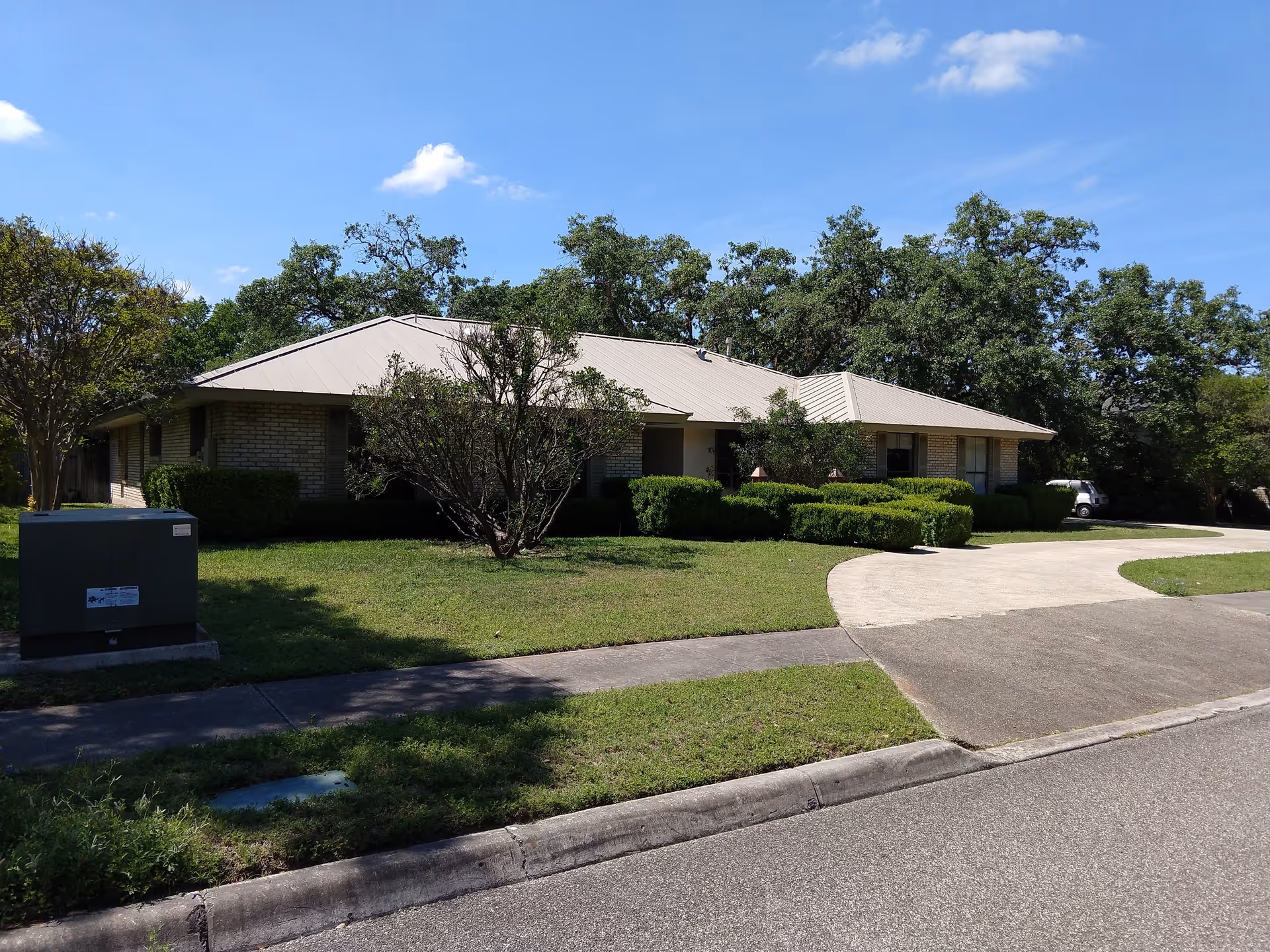 Single-story facility with a beige metal roof, curved driveway, and trimmed shrubs.