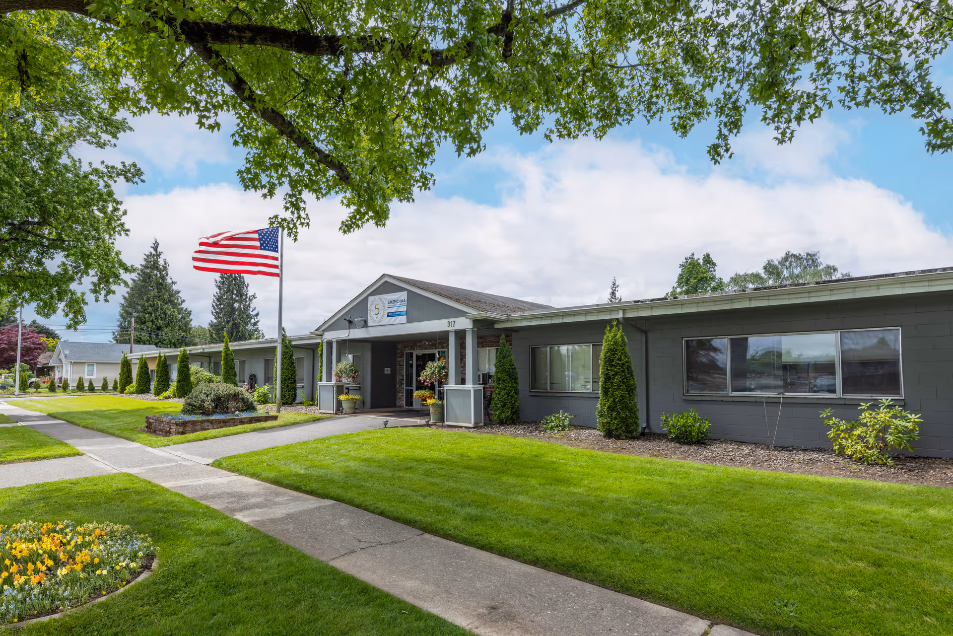 Exterior view of Americana Health & Rehab Center with lawn, walkway, and American flag.