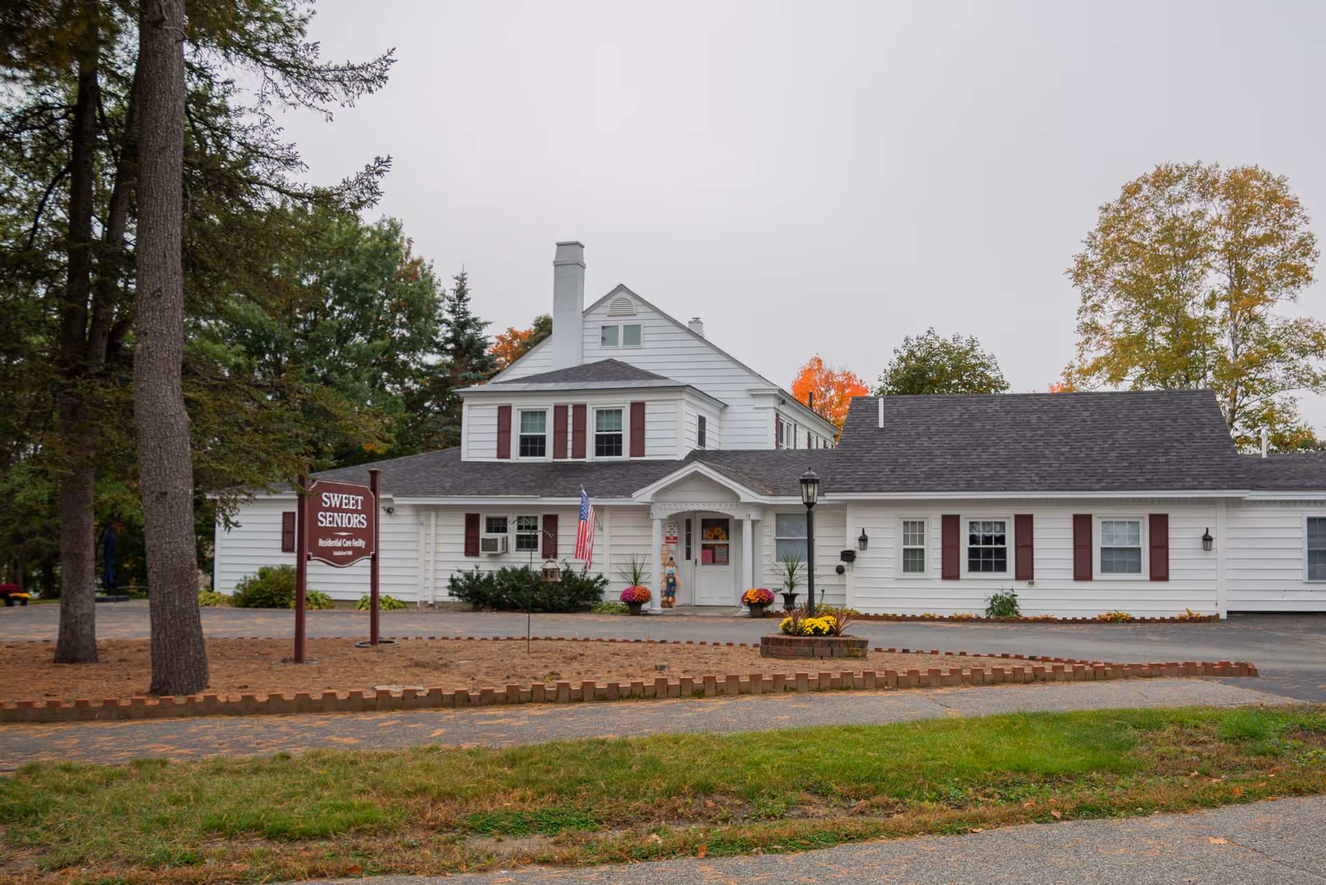 White, single-story senior living facility with a sign reading Sweet Seniors in a landscaped front yard