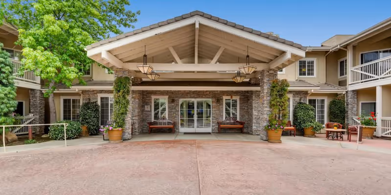 Front entrance of a senior living facility with stone pillars and planters in a courtyard.