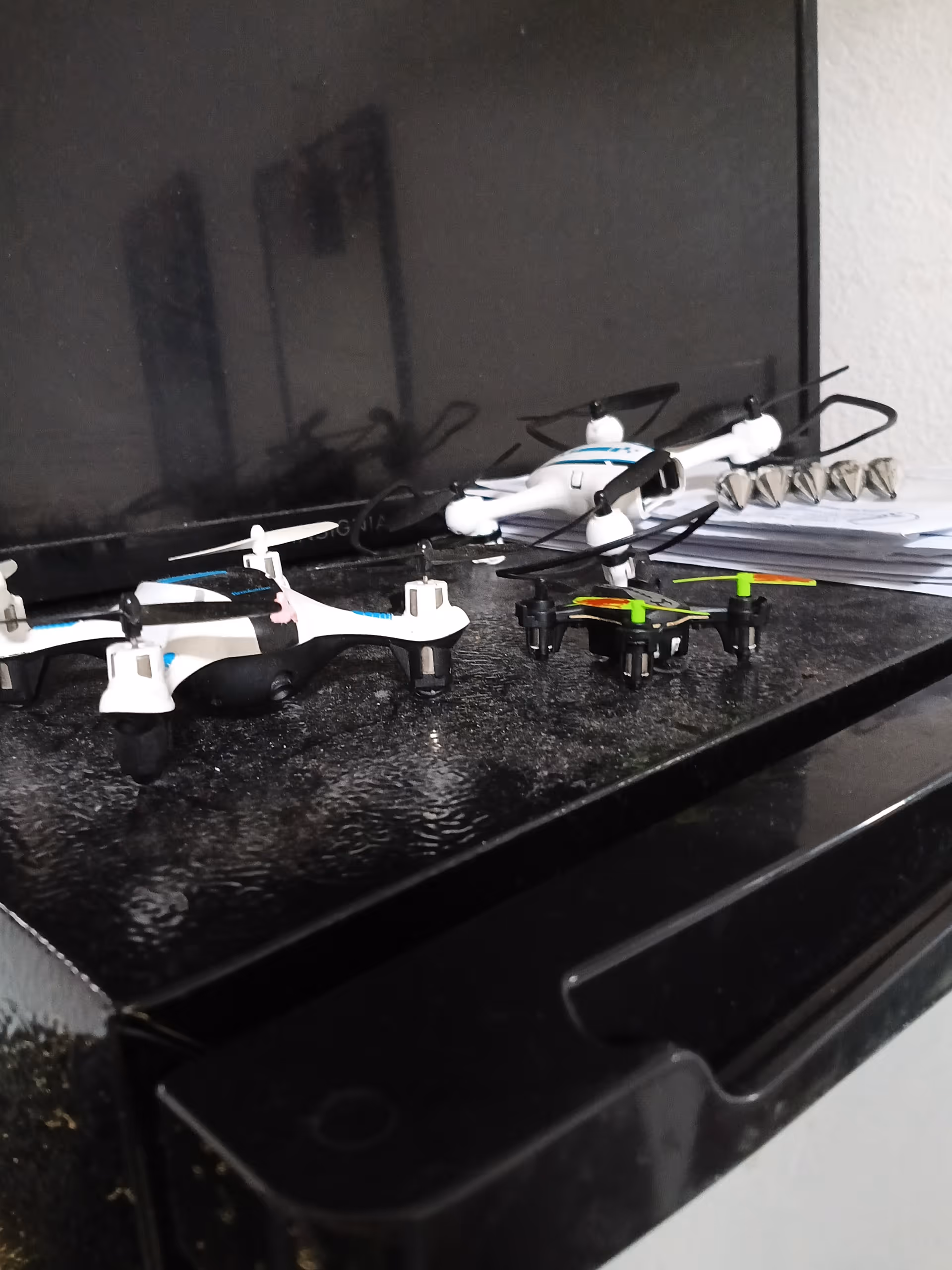 Several small drones sit on a dark shelf in front of a television.