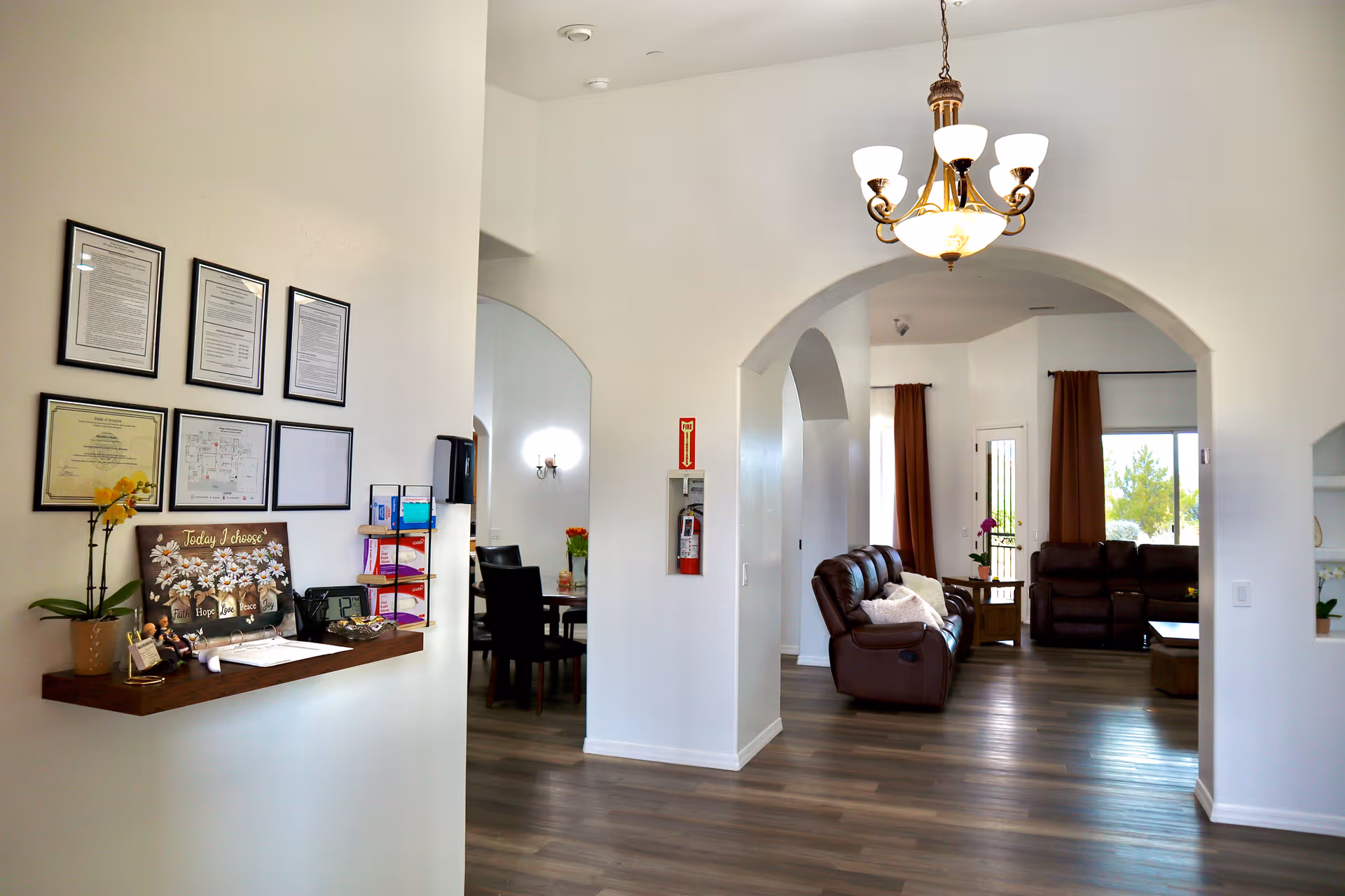 Bright senior living lobby with arches, chandelier, framed certificates, and leather seating.