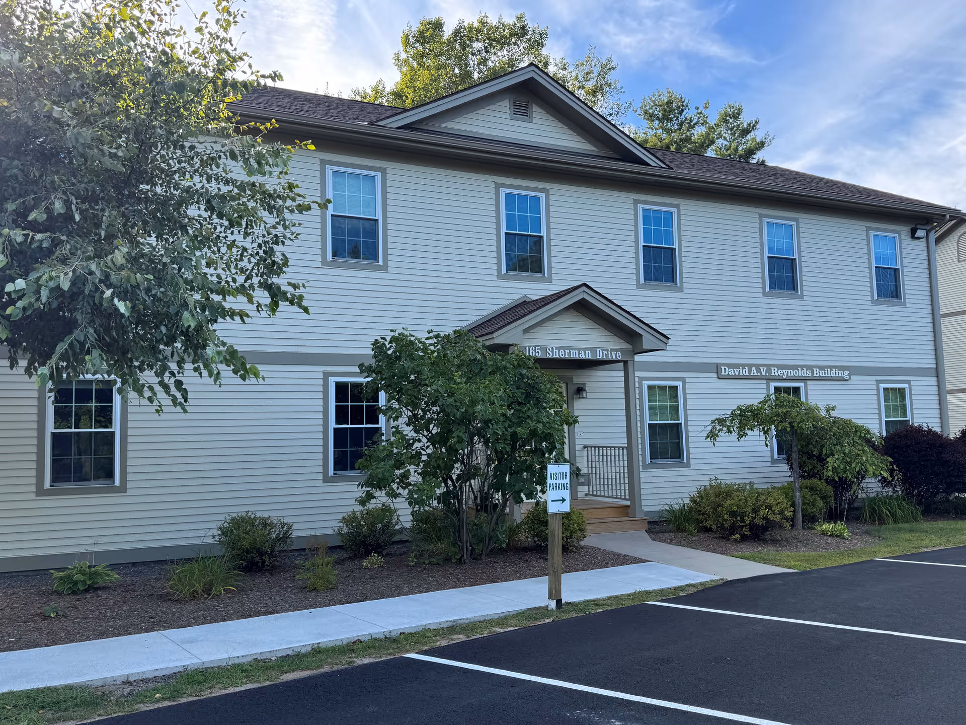 Two-story building exterior with entrance, parking lot, and landscaped surroundings.
