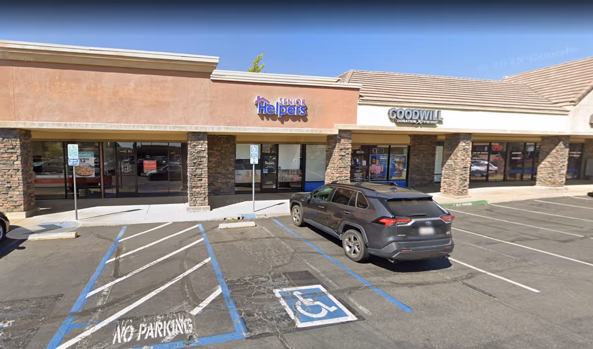 Exterior strip mall storefronts with Senior Helpers of Cameron Park and Goodwill, parked car in foreground.