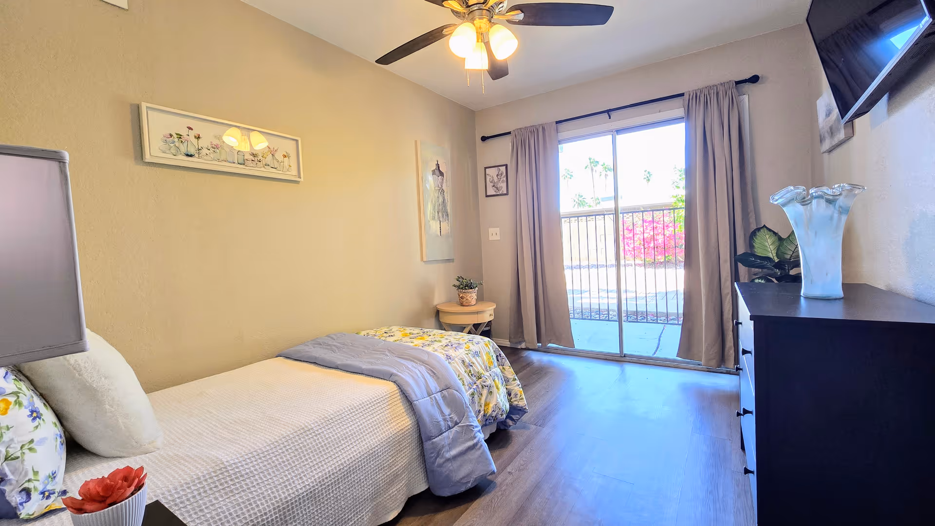 A bright bedroom with two twin beds, dresser, and sliding glass door to a balcony.