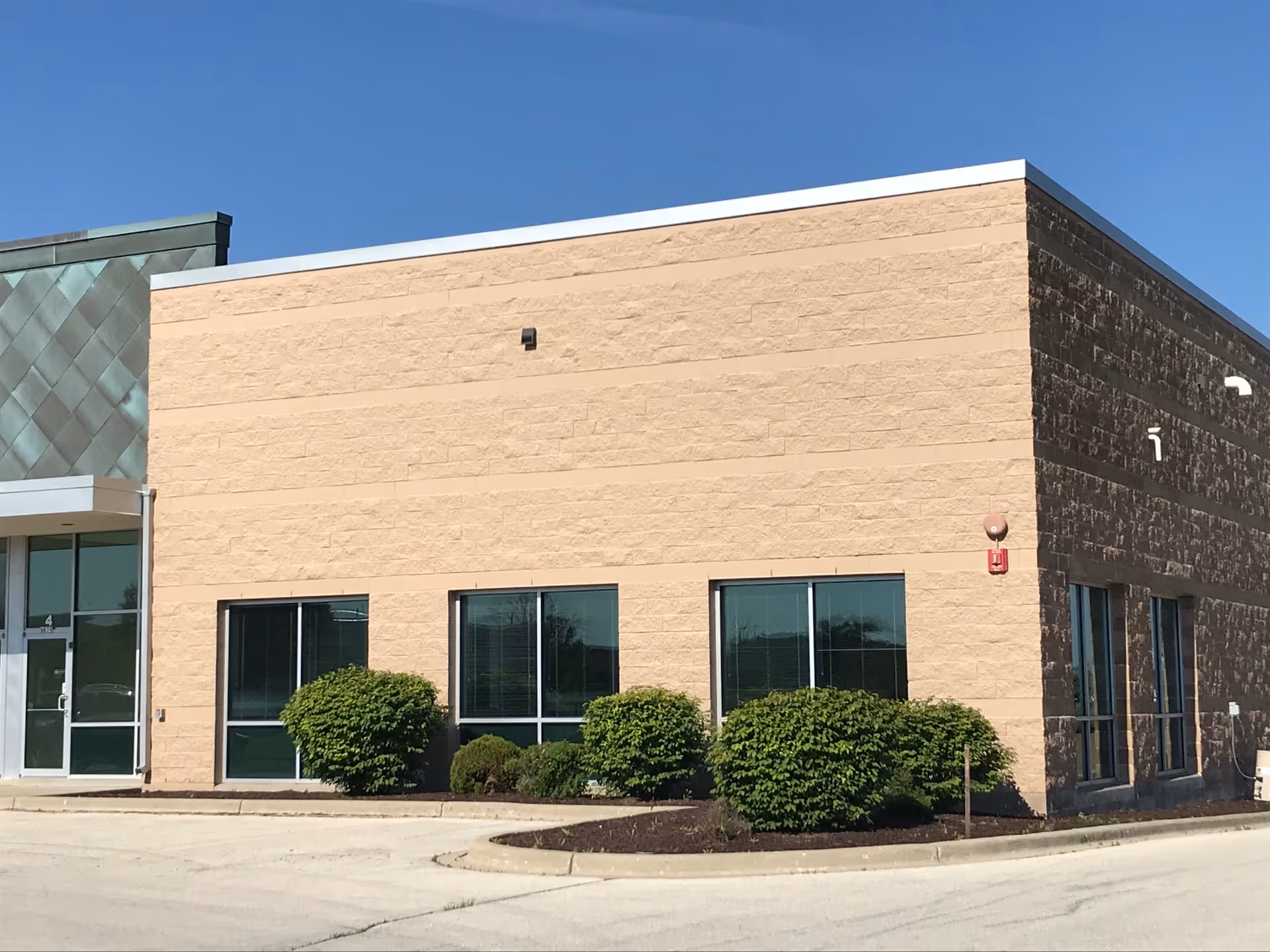 Exterior view of a tan brick senior living facility with shrubs and glass entry doors.