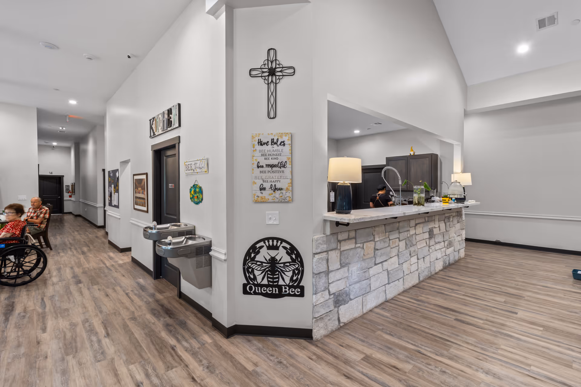 Bright interior lobby of a senior care home with a stone-front reception desk and residents nearby.