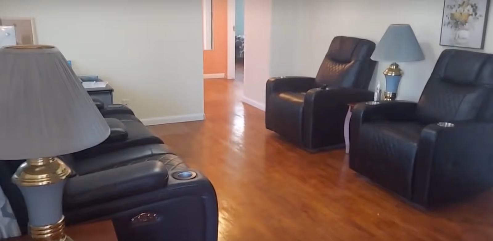 Spacious living room with black leather recliners, a sofa, wooden floor, and lamps.