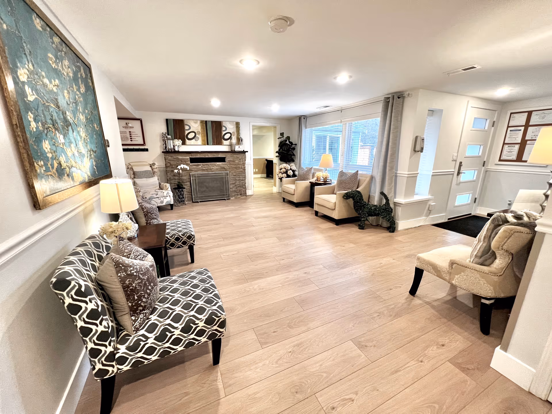Spacious senior living facility lounge with fireplace, seating, and large front windows.
