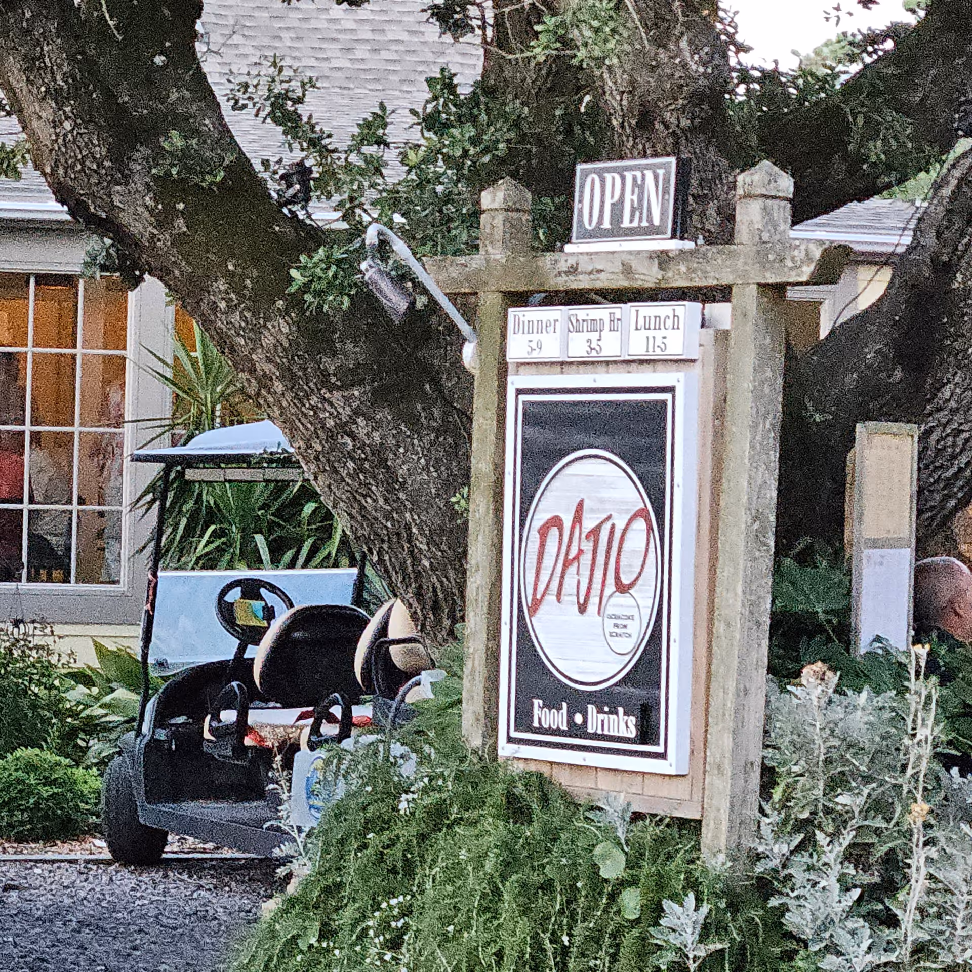 Open sign with a wooden frame and a large circular logo outdoors beside a golf cart.