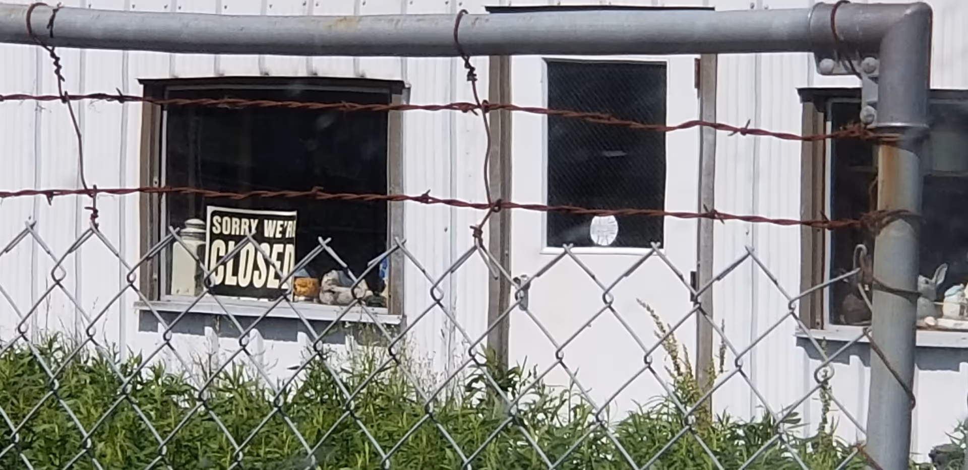 Front view of a white building with barred windows, chain-link fence, and a 'closed' sign.