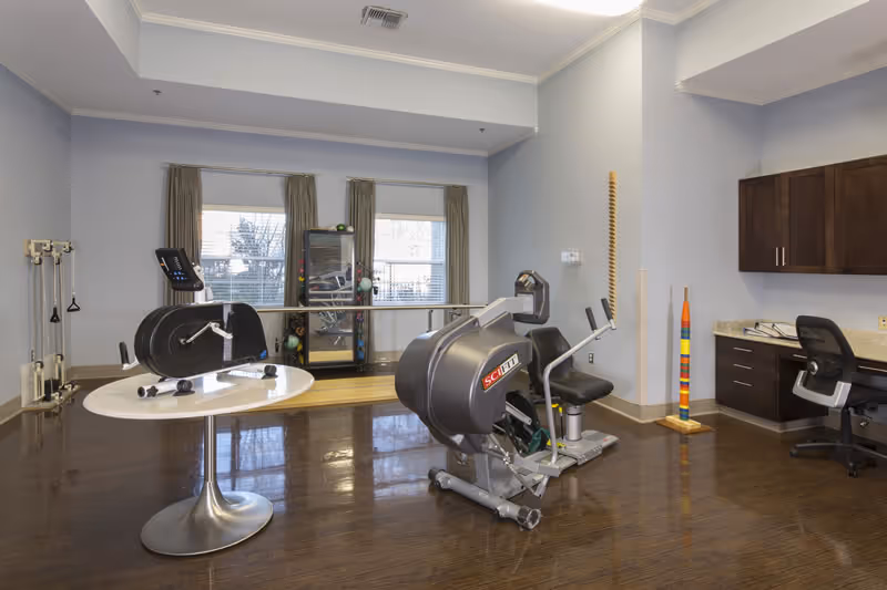 Interior exercise room in a senior facility with cardio equipment and a desk.